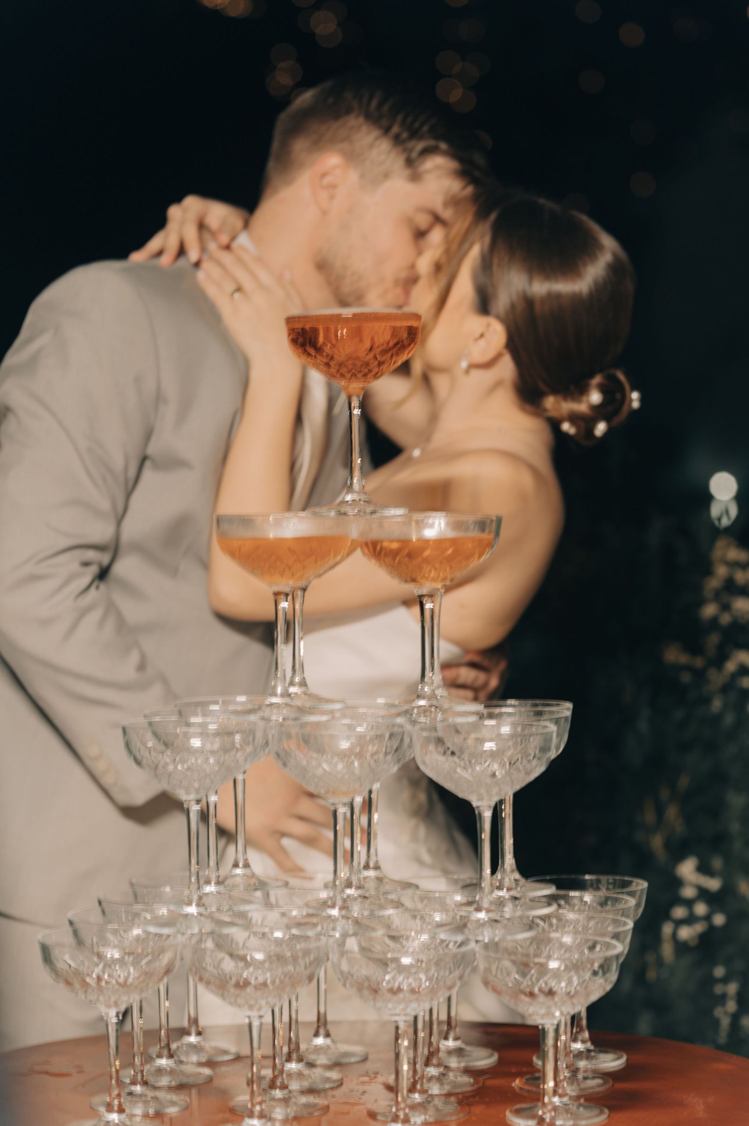 Couple shares intimate moment behind champagne tower at wedding reception.