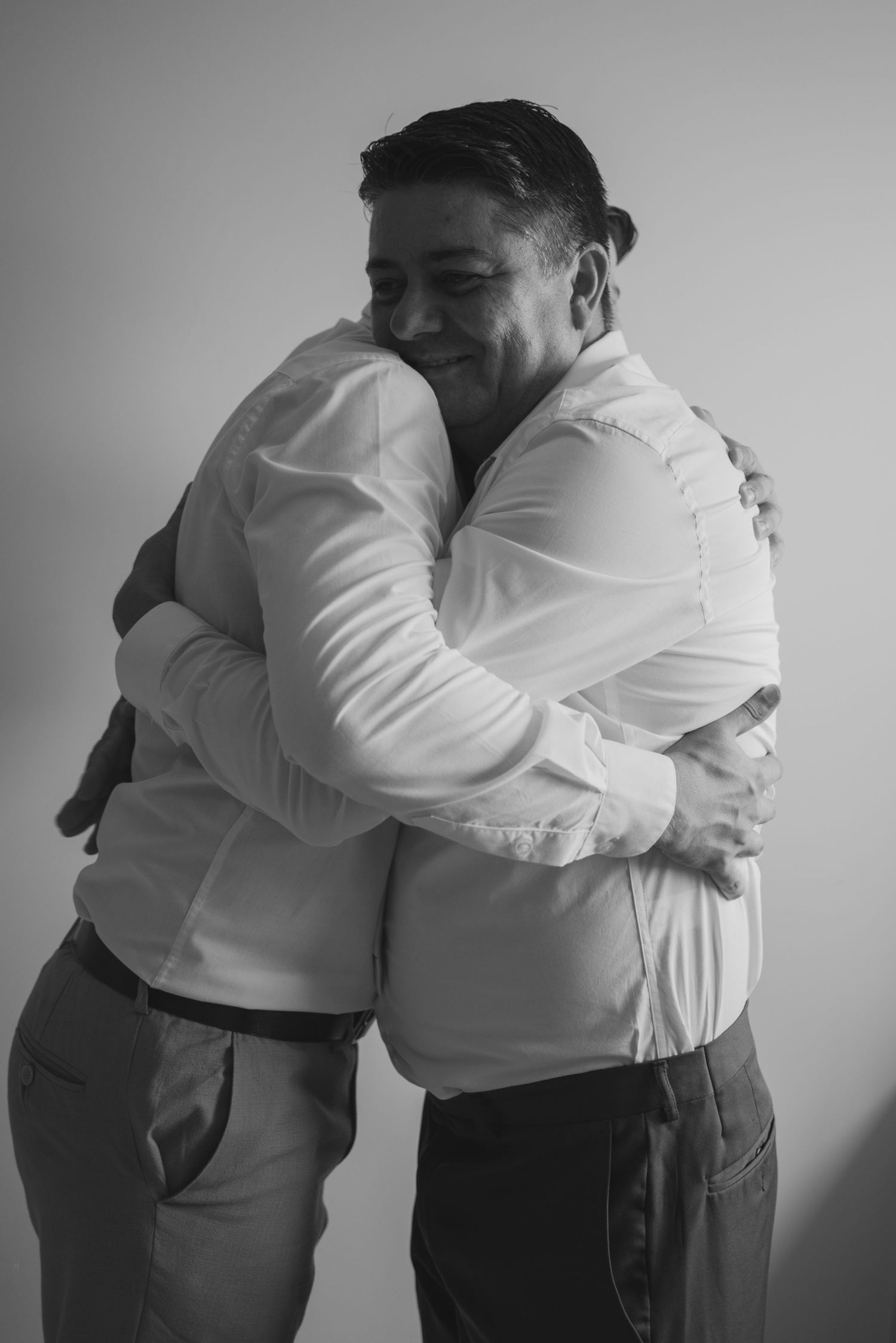 Two people in white shirts and grey pants sharing a warm embrace.