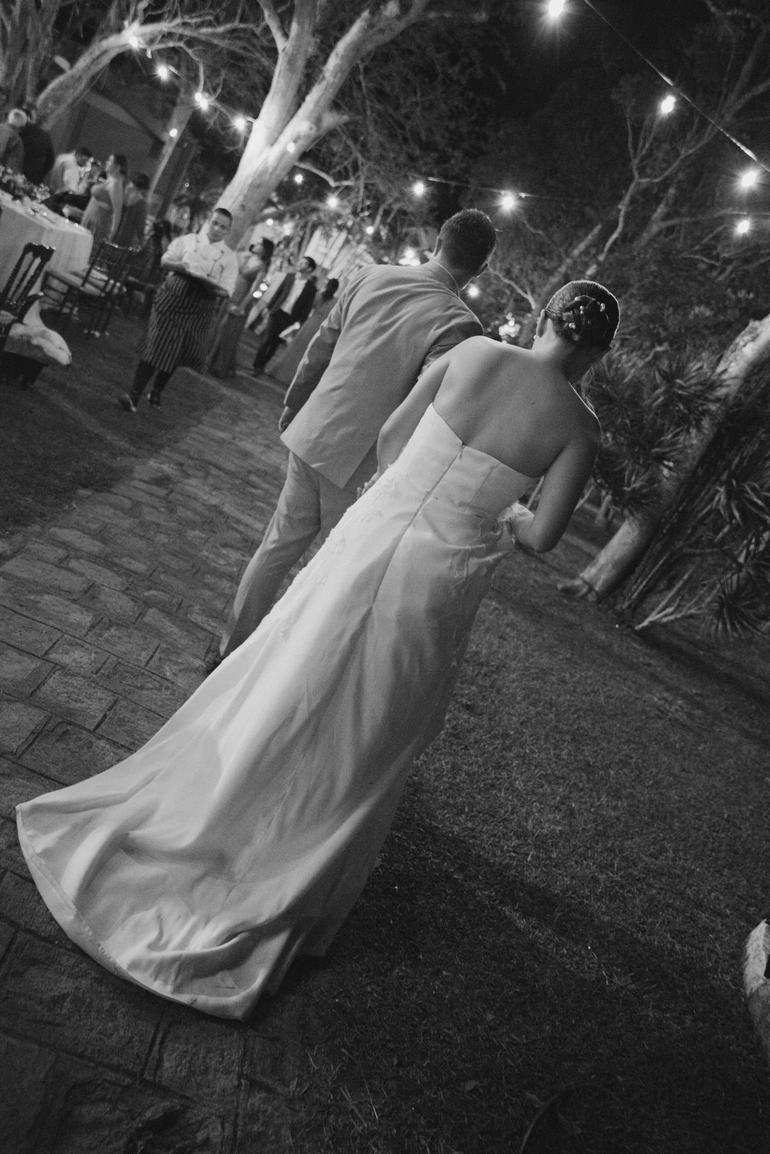 A couple dancing at an outdoor wedding reception with string lights illuminating the garden setting.