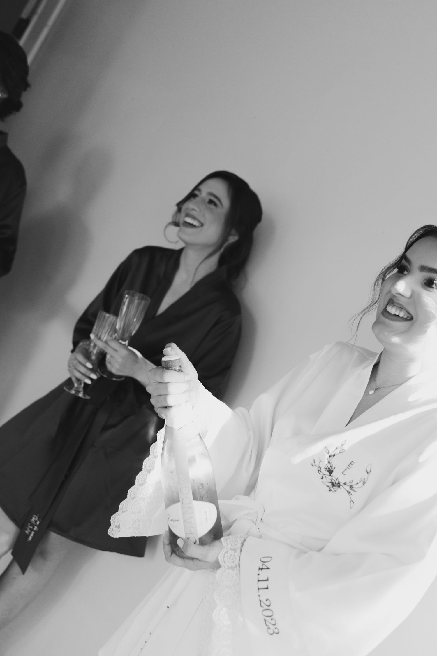 Joyful pre-wedding preparation moment with robes and champagne in black and white.