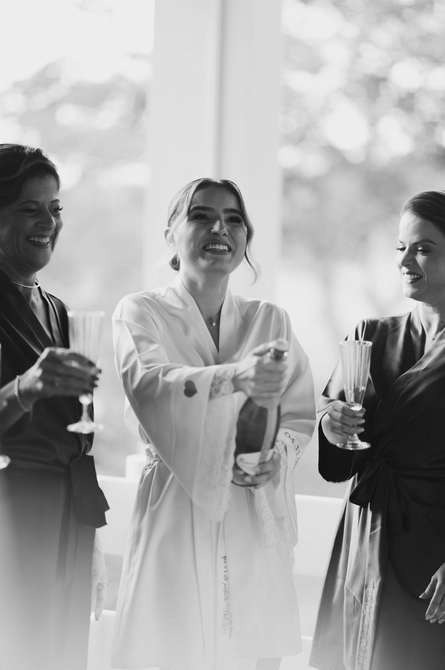 Candid black and white photo of wedding party members sharing laughter and drinks.