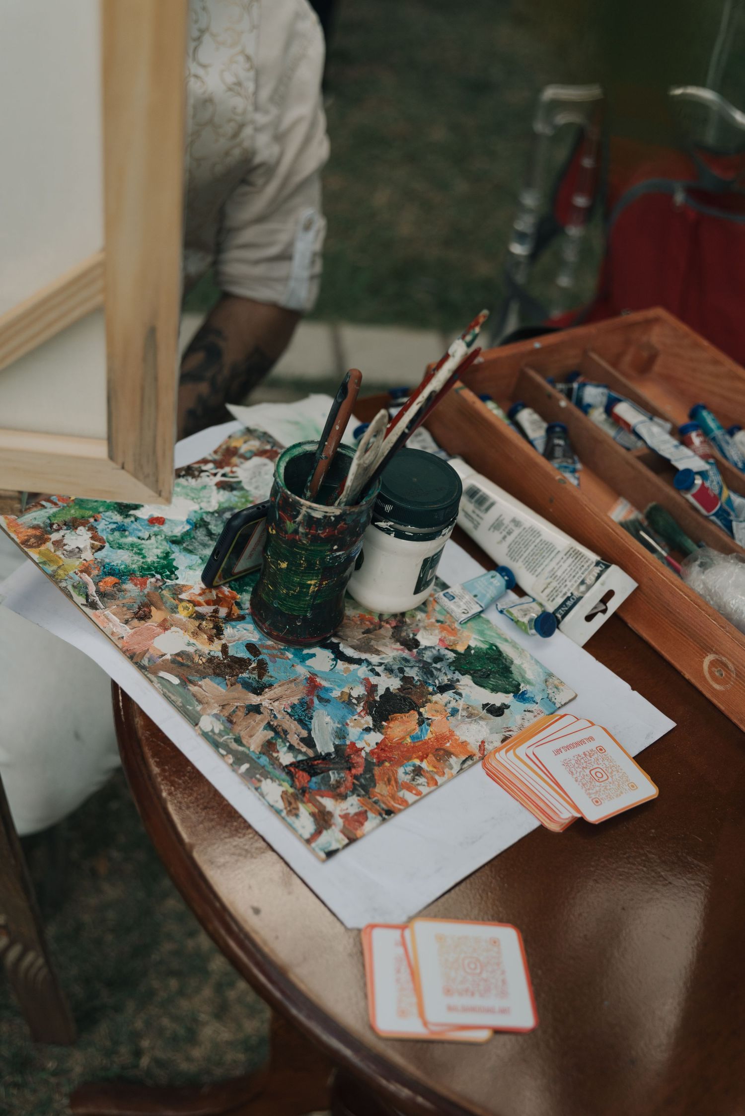 Artist's workspace with paint palette, brushes and art supplies arranged on wooden table.