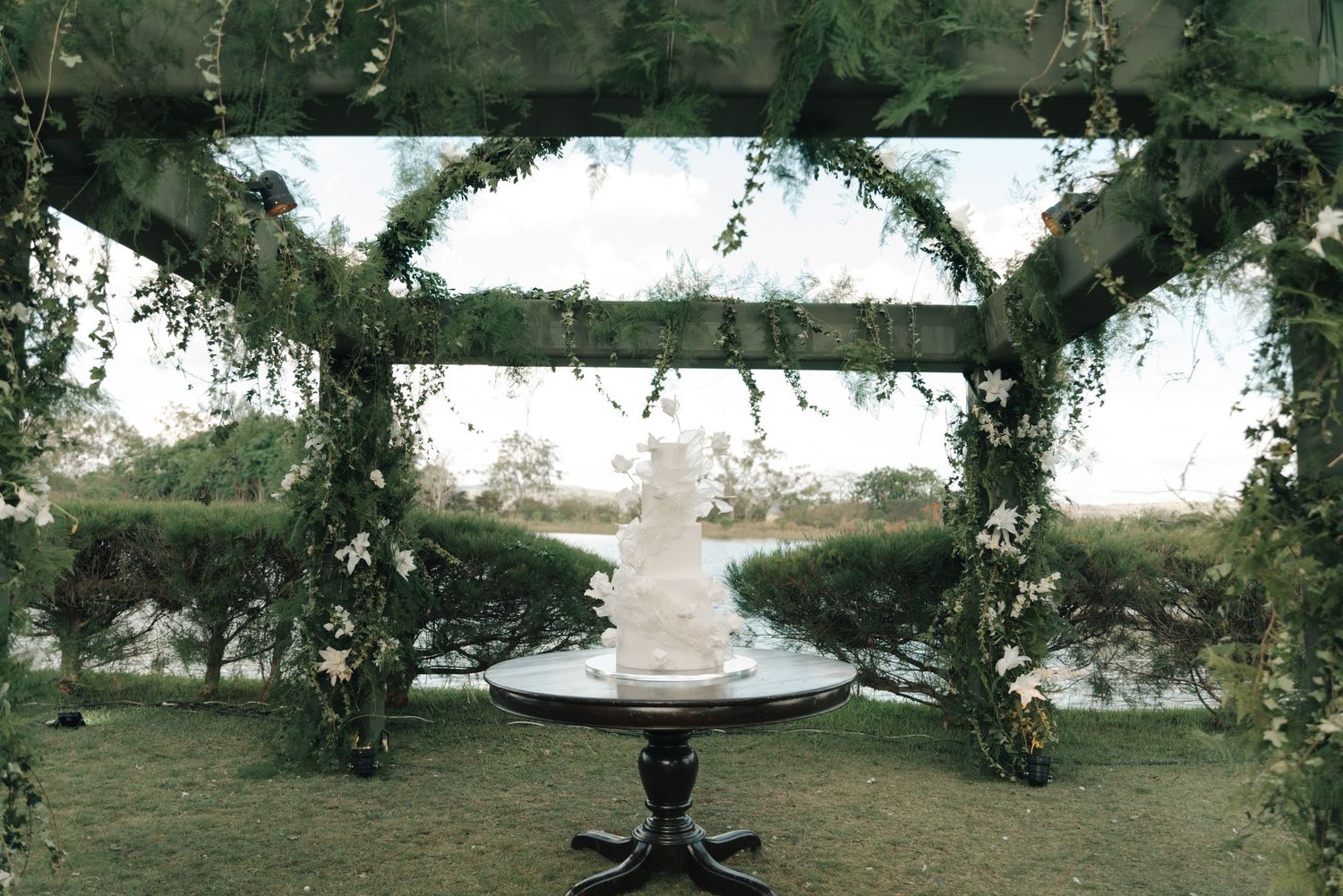 Wedding cake display under a greenery-covered arch with garden scenery.