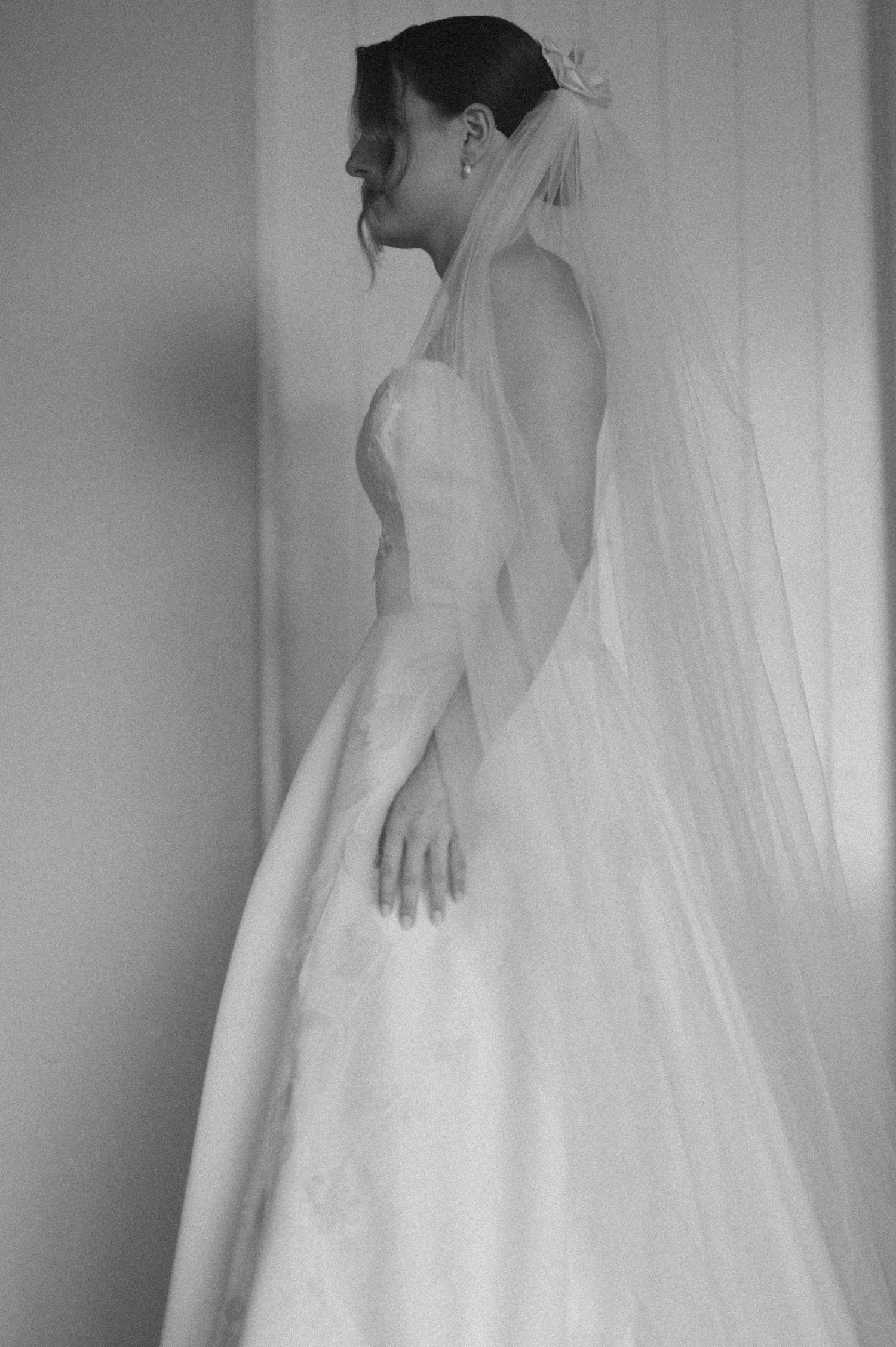 Side profile of classic white wedding gown with flowing veil in black and white.