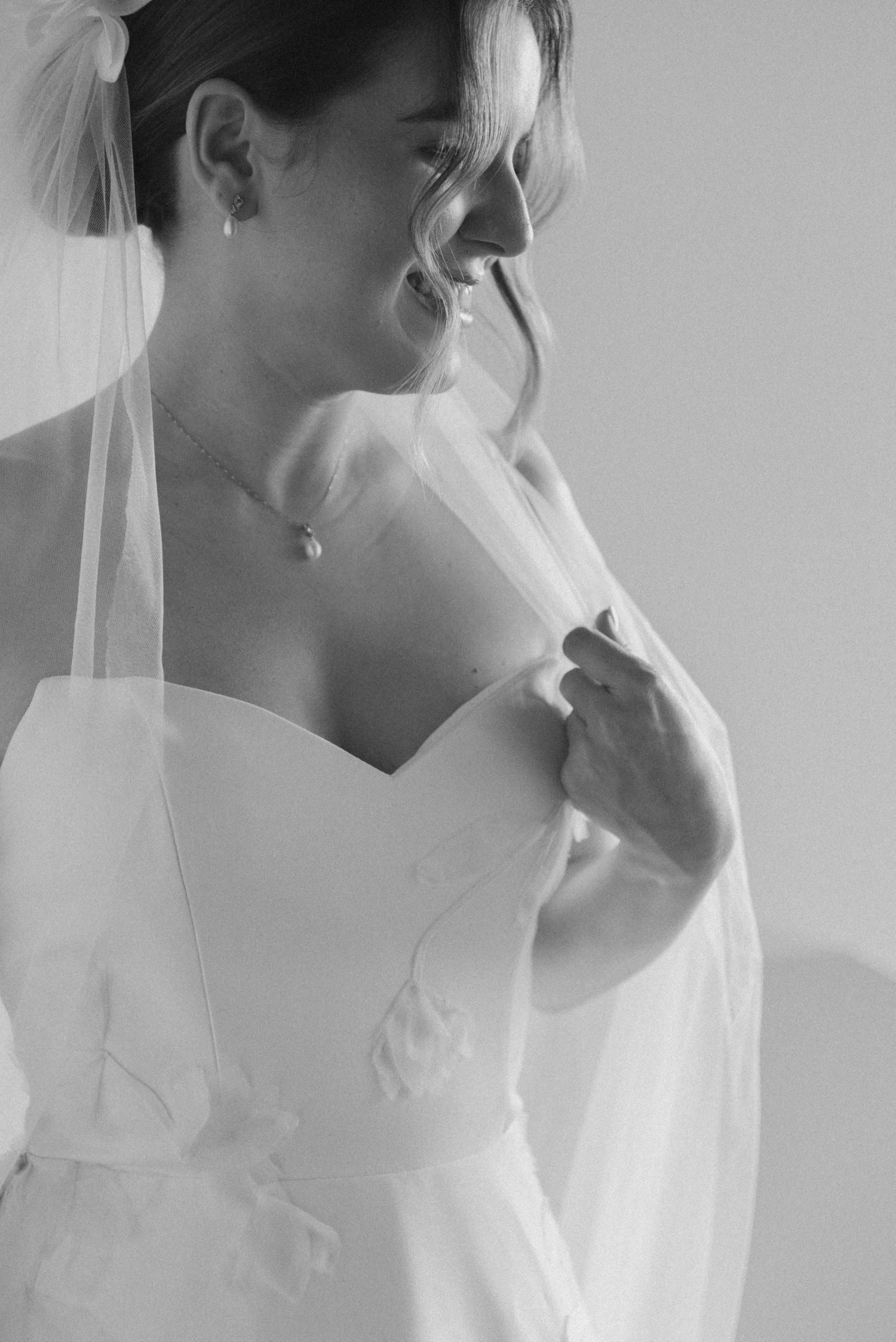 Close-up black and white photo of a bride in a sweetheart neckline dress adjusting her neckline.