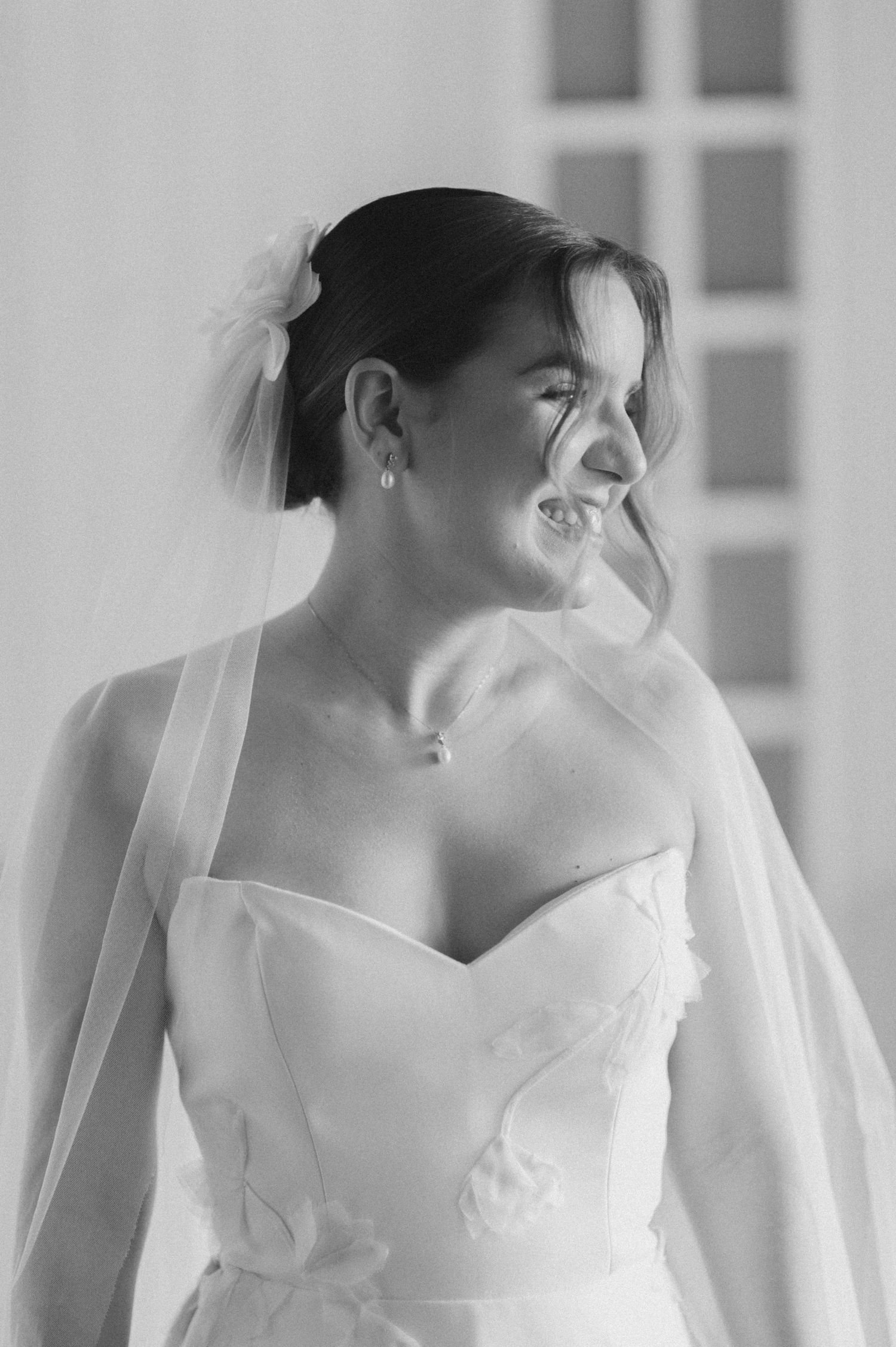 Candid black and white photo of a joyful bride in a strapless wedding dress and veil.
