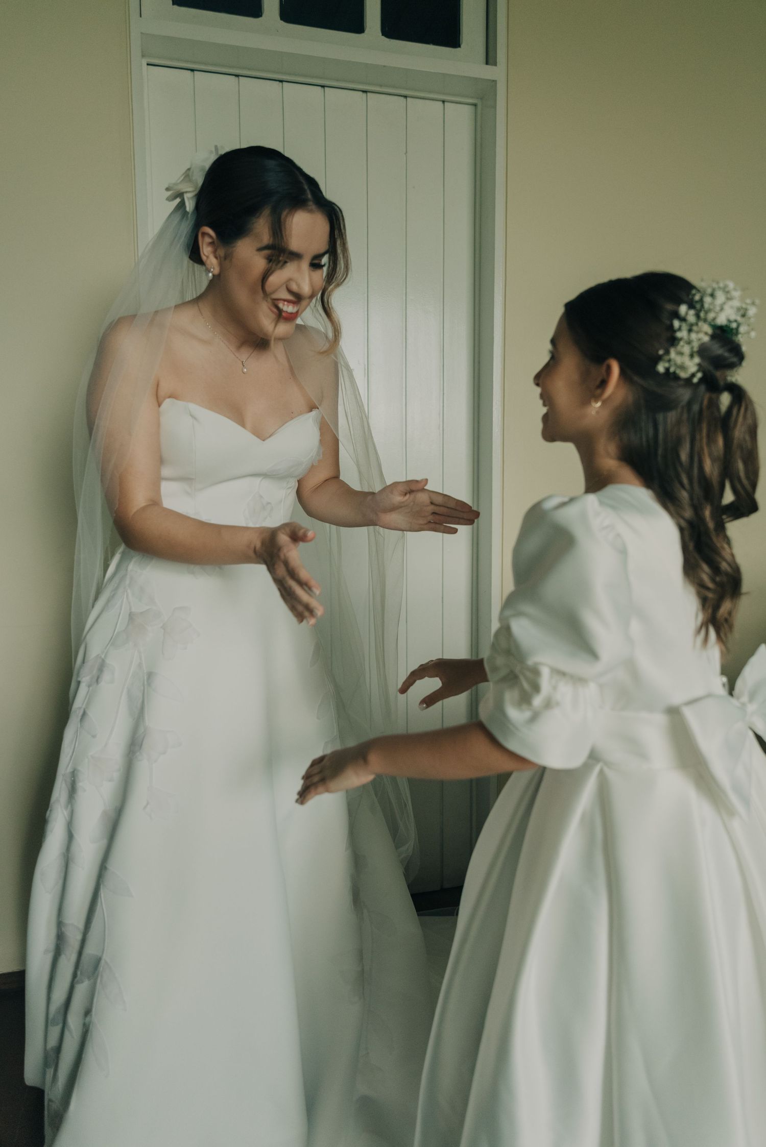 Candid moment of bride and young attendant in white dresses sharing laughter together.
