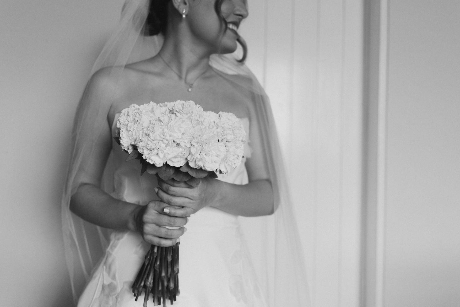 Black and white photo of bride holding white flower bouquet in classic wedding dress.
