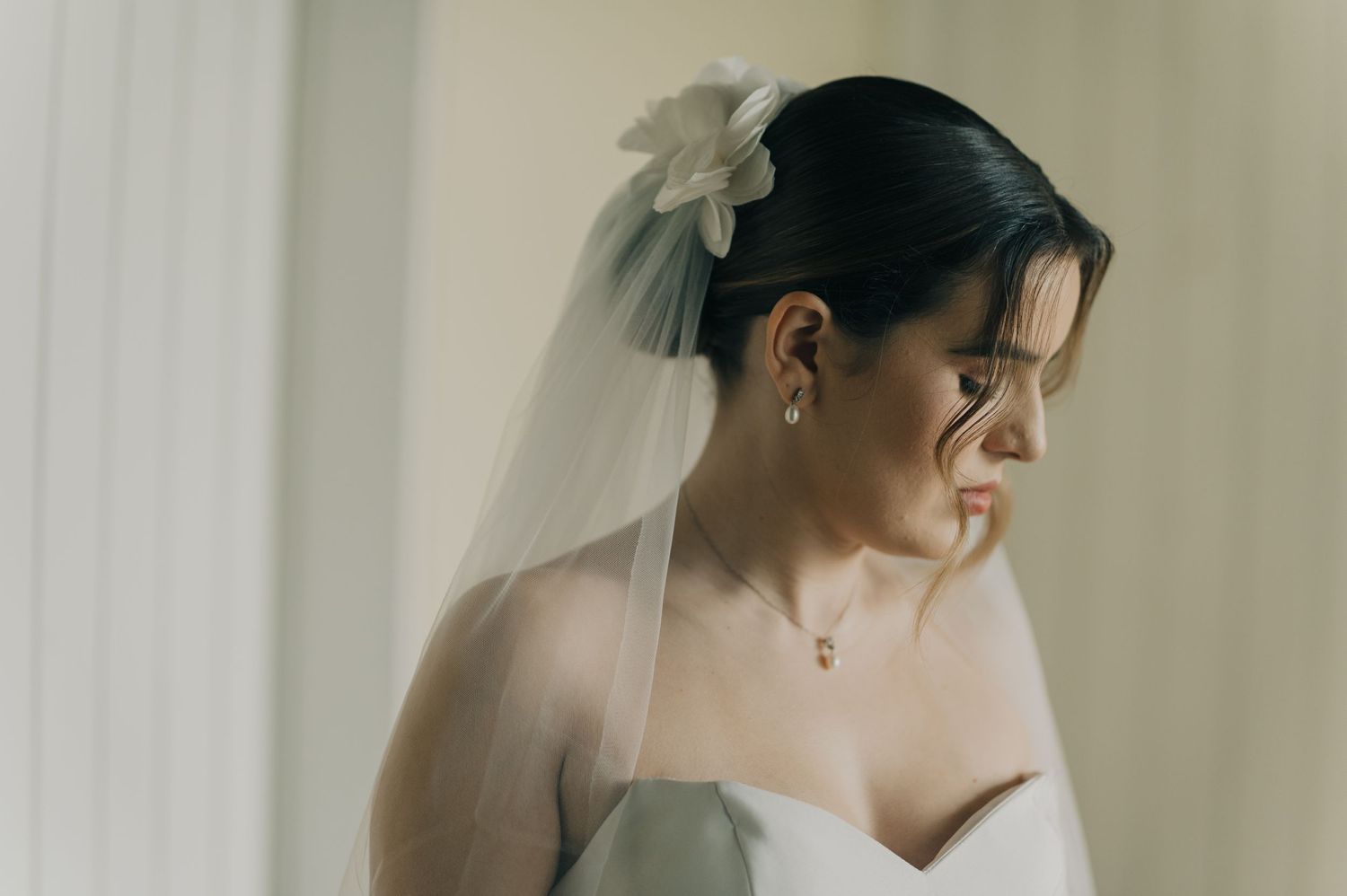 Close-up portrait of bride in strapless gown with delicate veil and floral hair accessory.