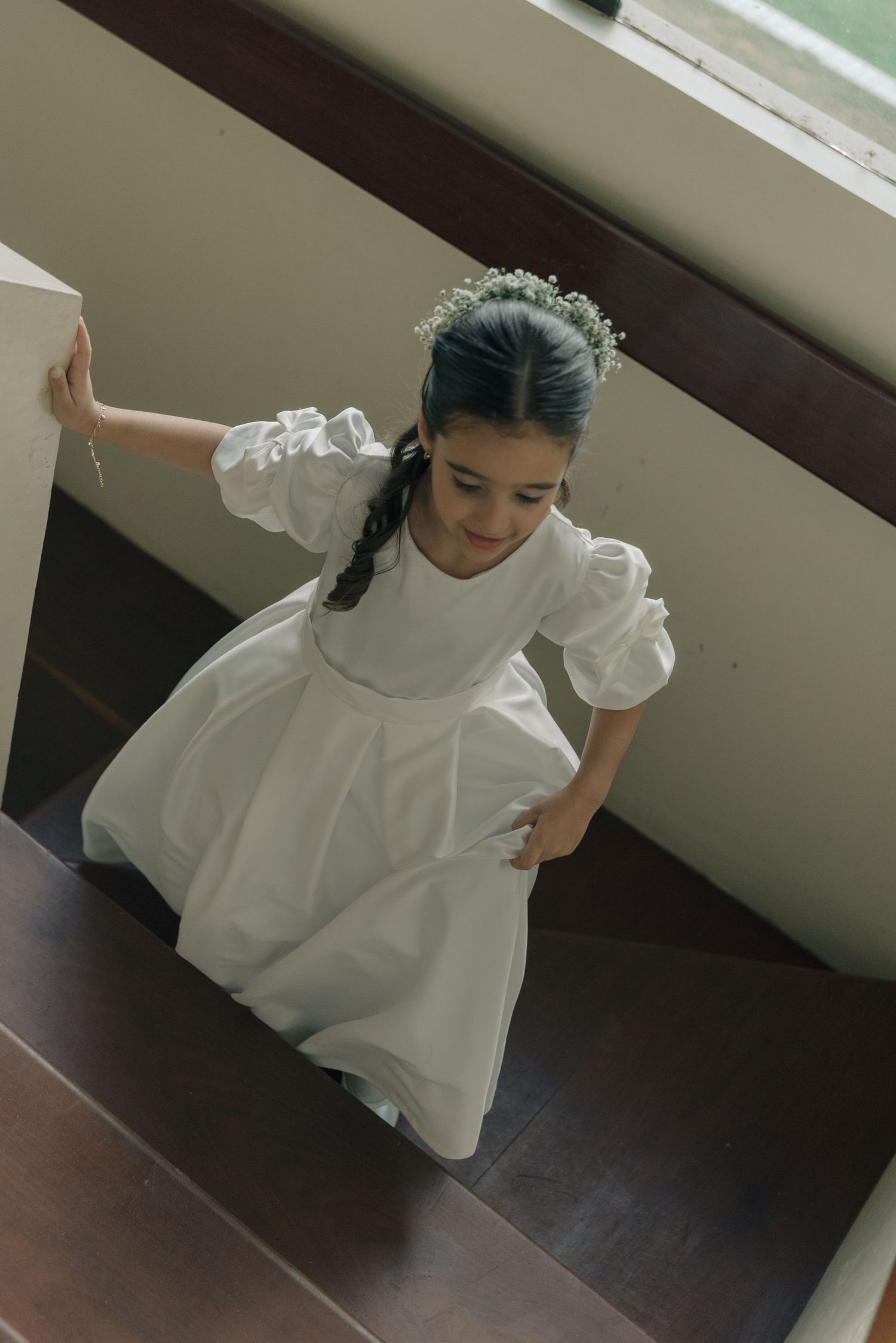 Young attendant in white dress with puff sleeves climbing stairs in an elegant setting.