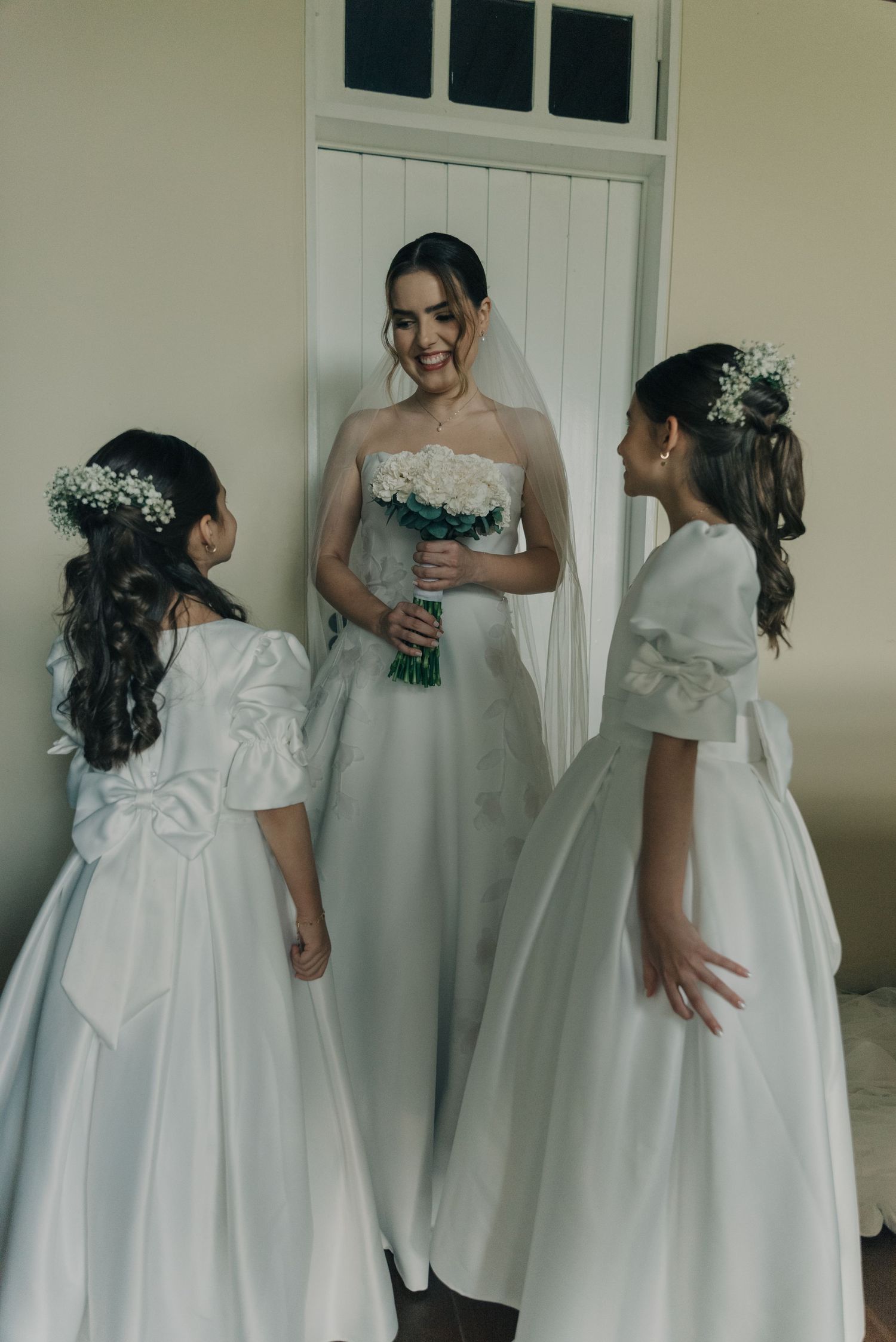 Bride in strapless gown with bouquet sharing a moment with two young attendants in white dresses.