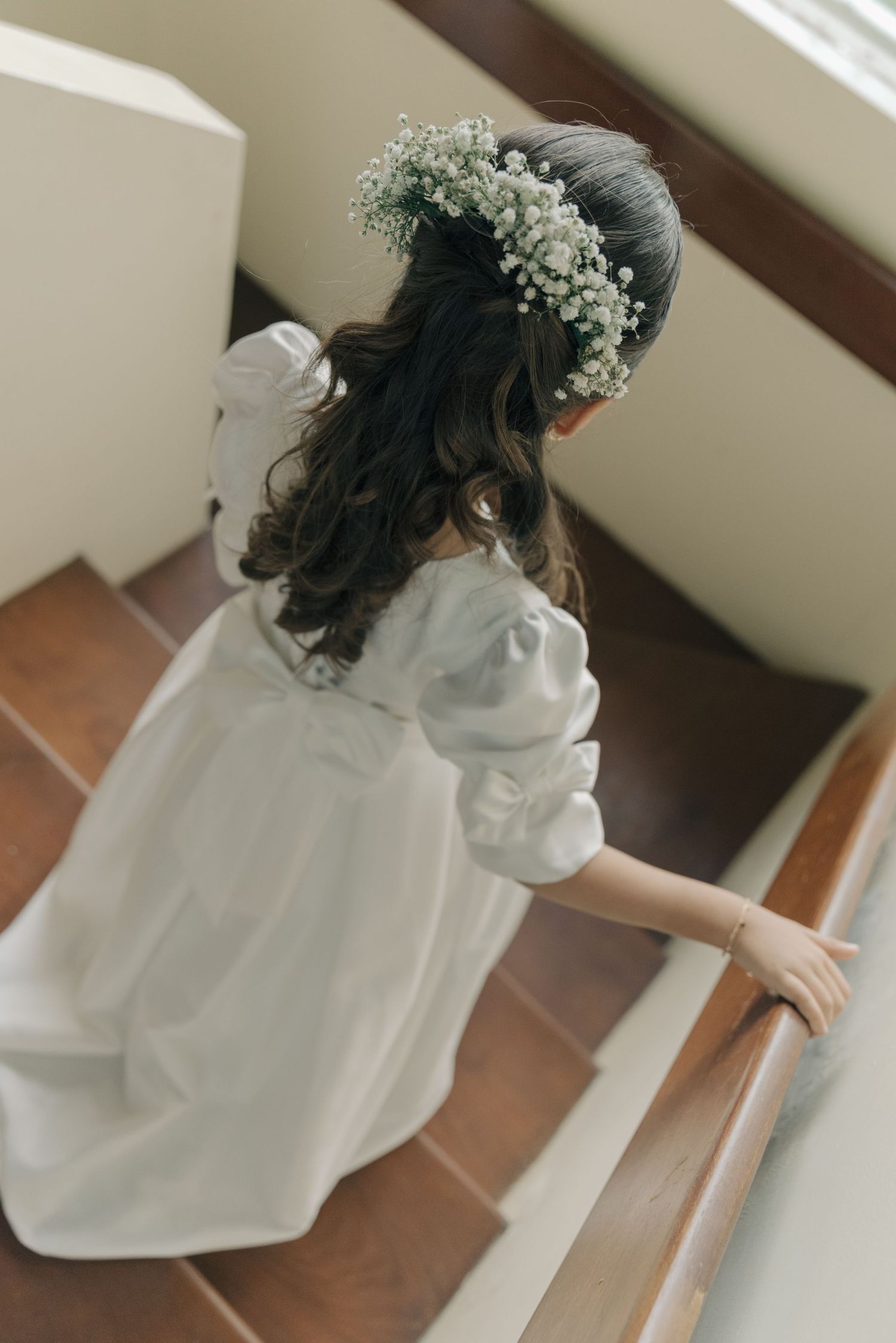 A figure descends stairs wearing a white dress and baby's breath flower crown.