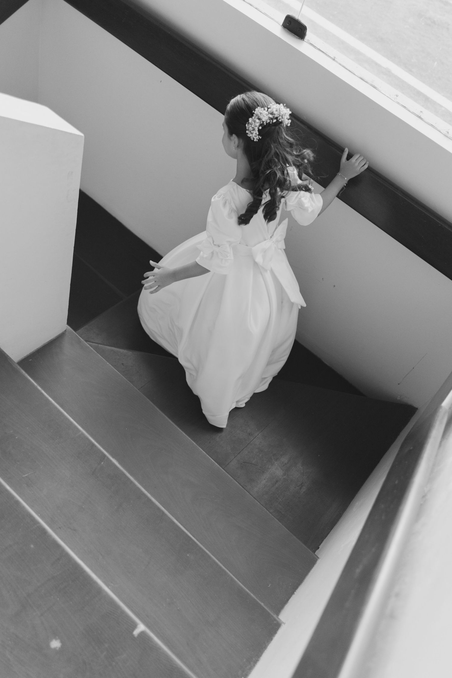 A person in a white dress walks down modern stairs, photographed from above in black and white.