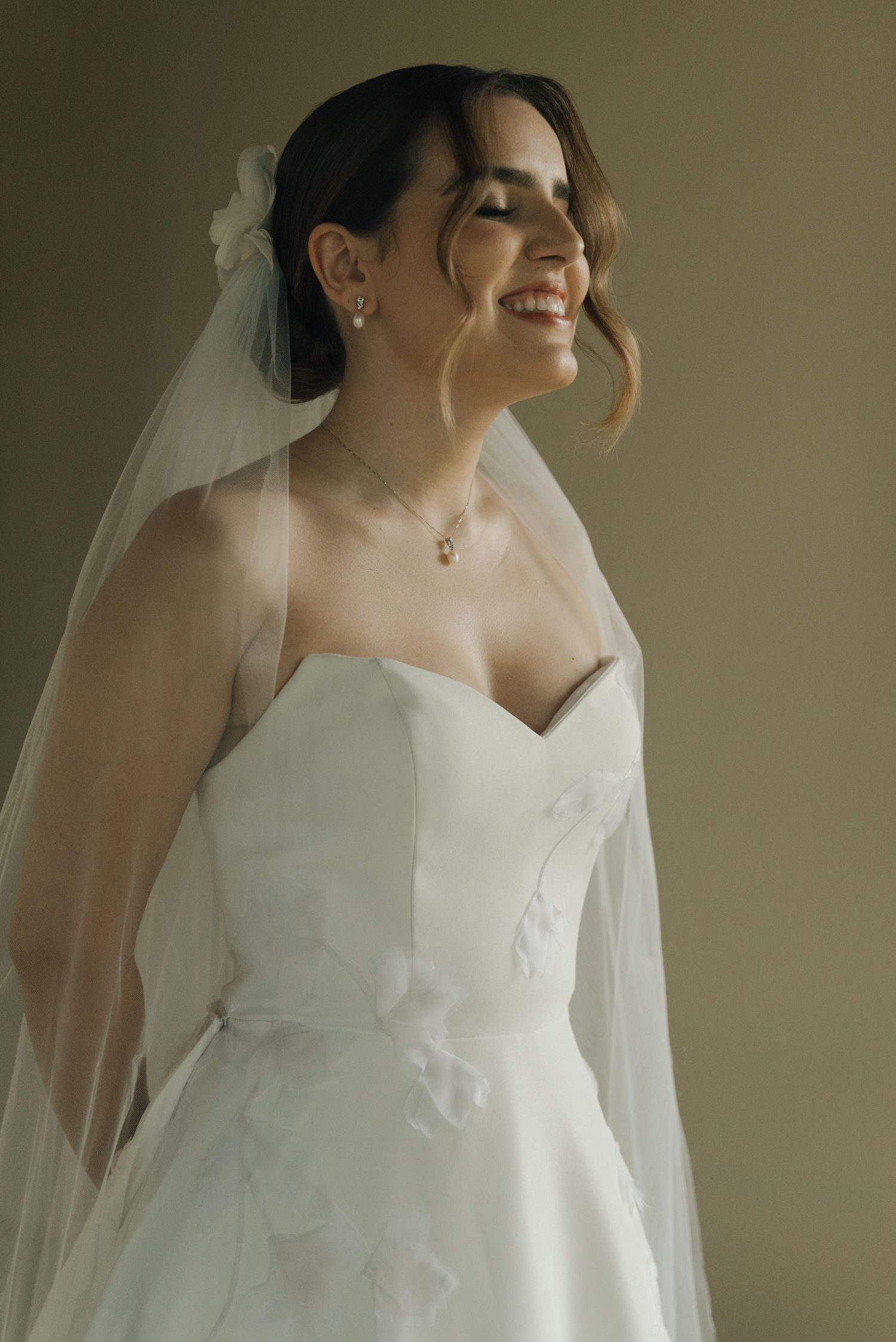 A joyful moment captured of a bride in a strapless white gown and delicate veil.