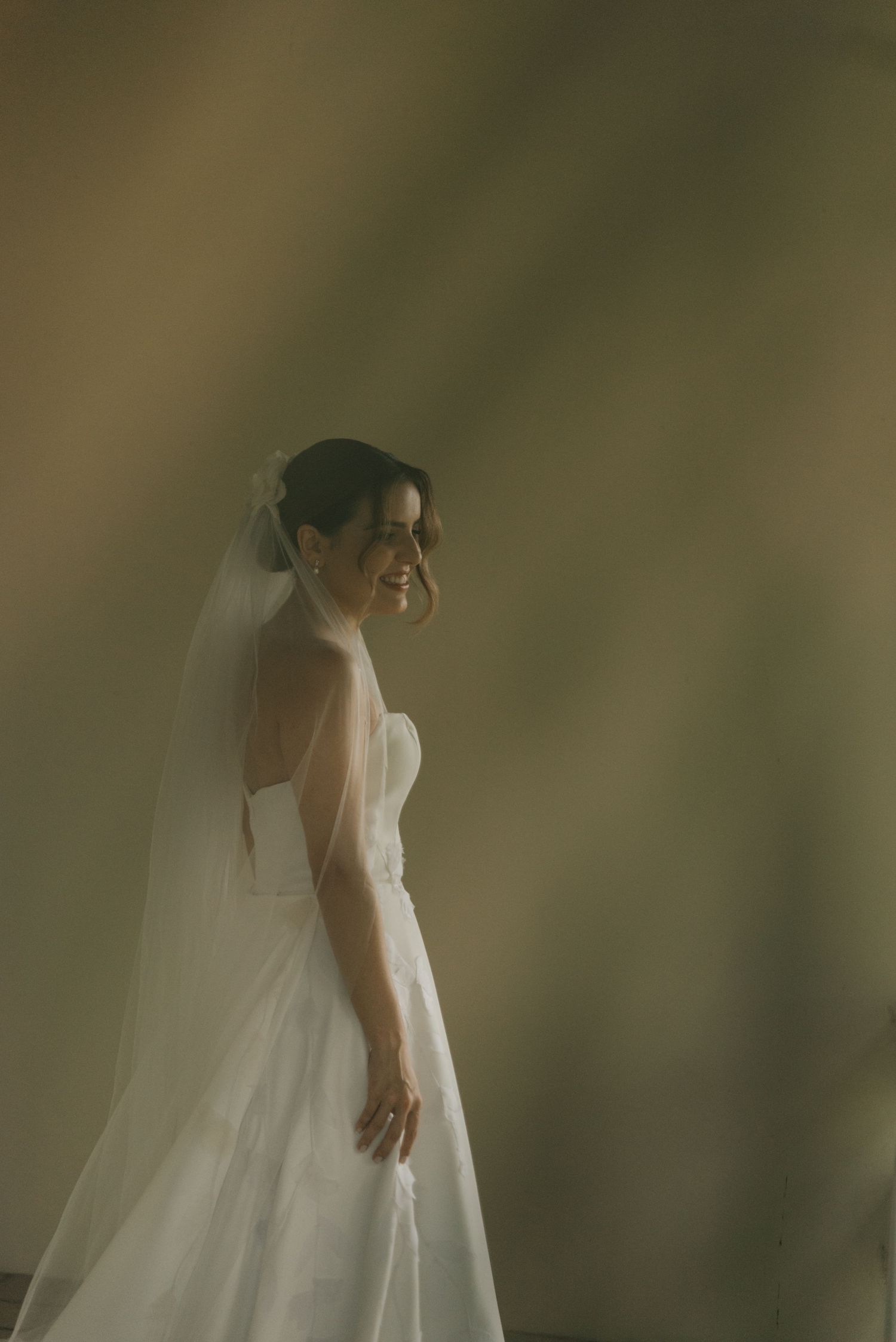 A candid side view of a bride in a strapless wedding dress against a soft background.