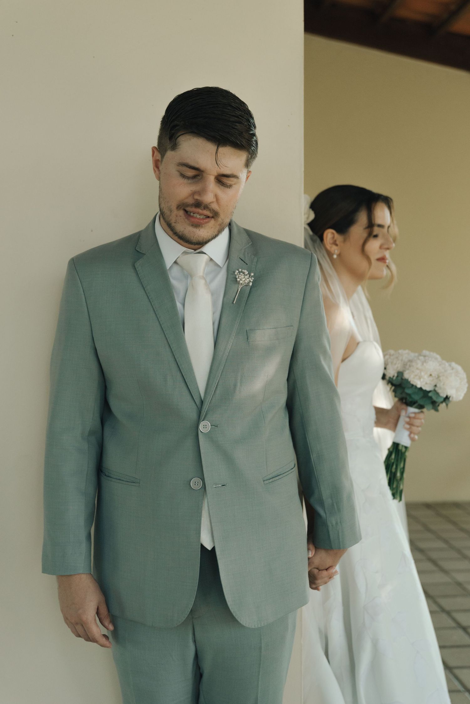 Wedding couple pose together, groom in sage suit and bride in white dress.