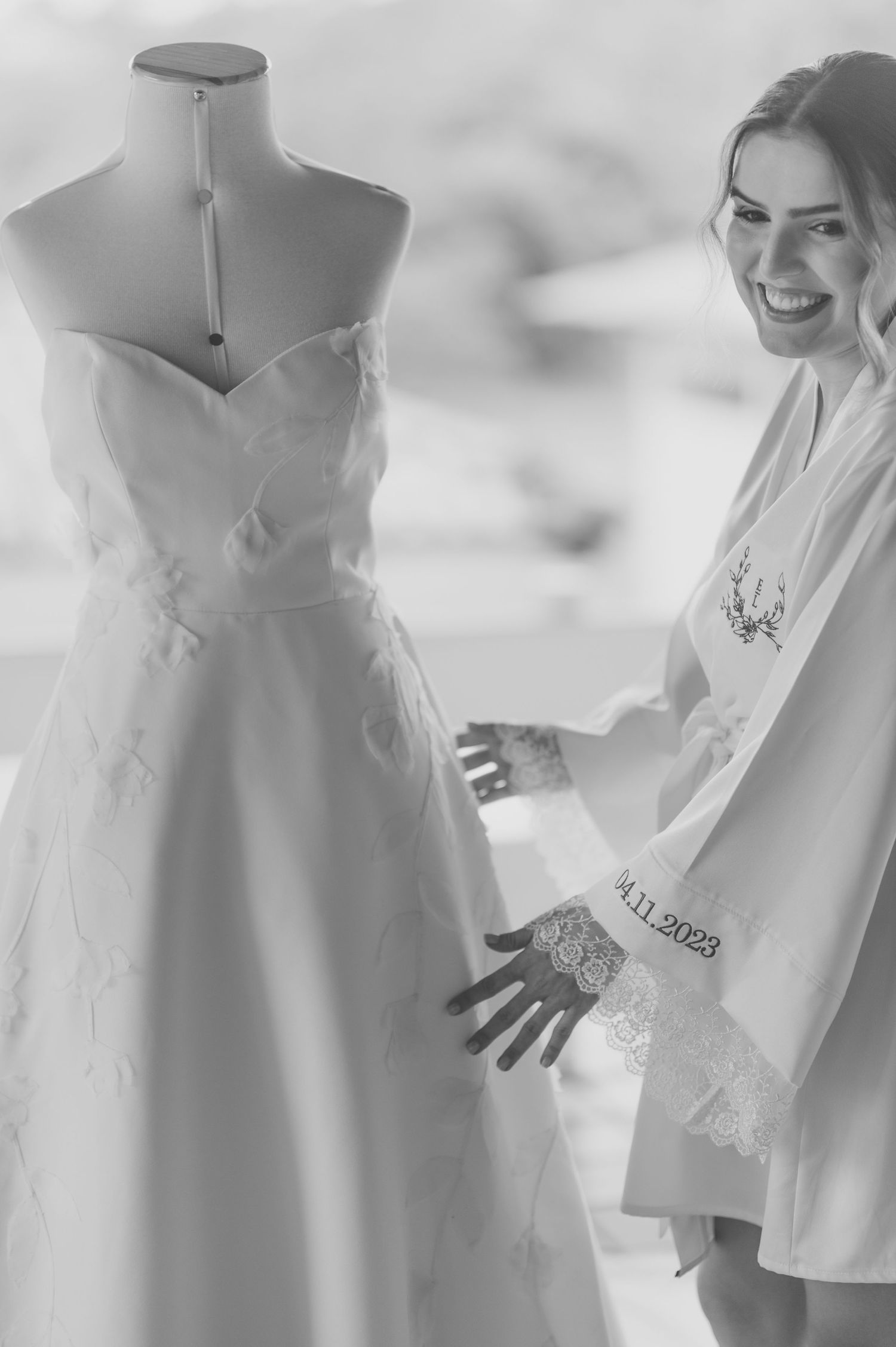 Wedding dress displayed on mannequin with person in white robe admiring it.