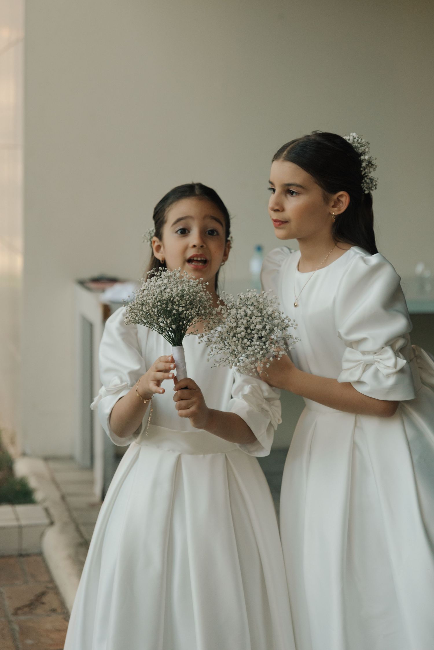 Two flower girls in white dresses holding baby's breath bouquets.