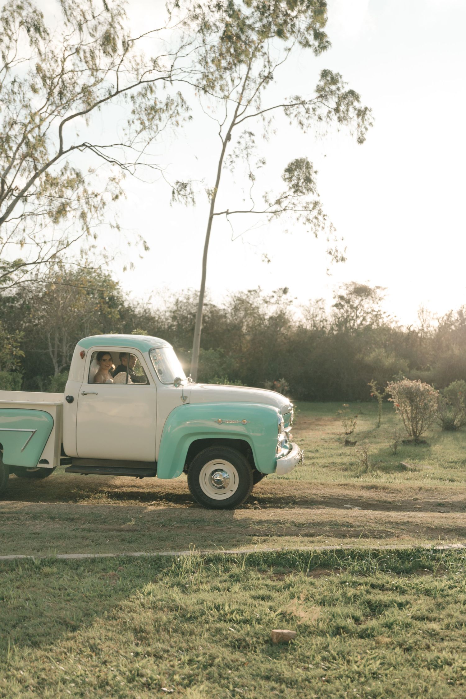 A classic turquoise and white pickup truck photographed in a rustic outdoor setting at sunset.