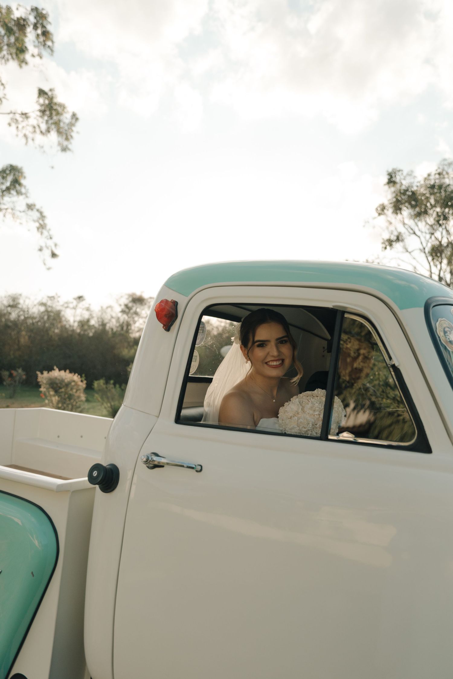 A vintage turquoise and white pickup truck with a passenger in bridal wear.