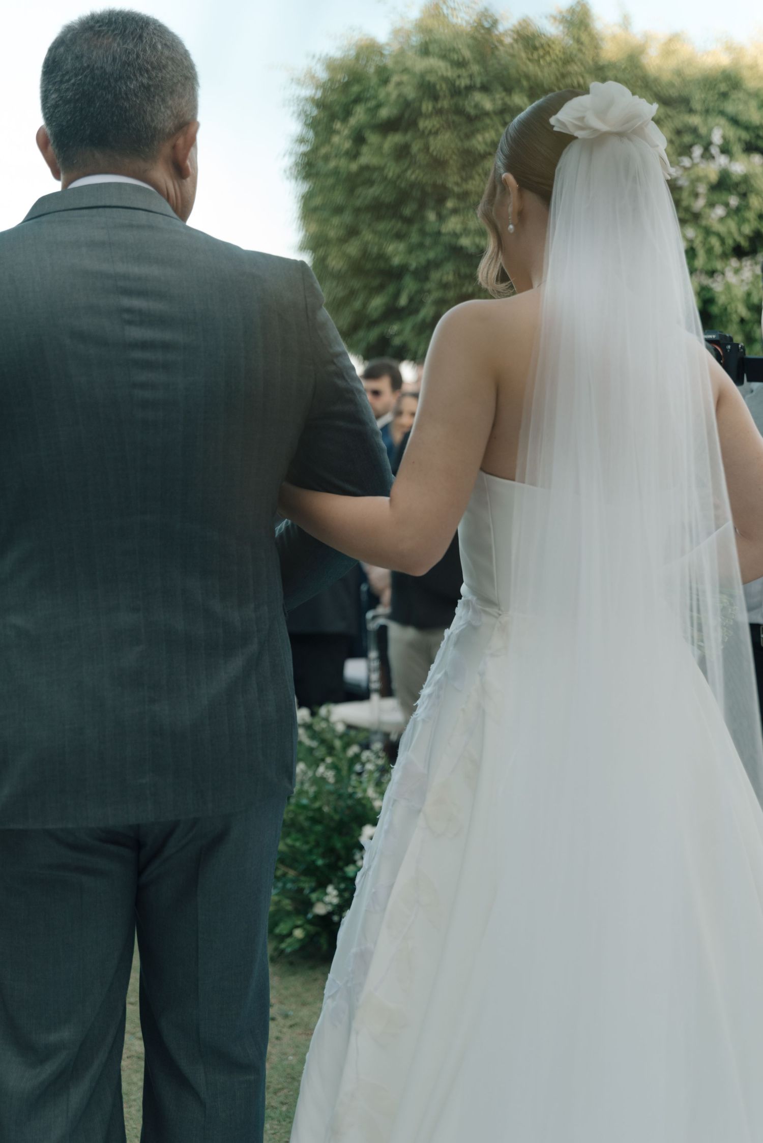 A wedding ceremony moment captured from behind showing the bride in a flowing white gown.