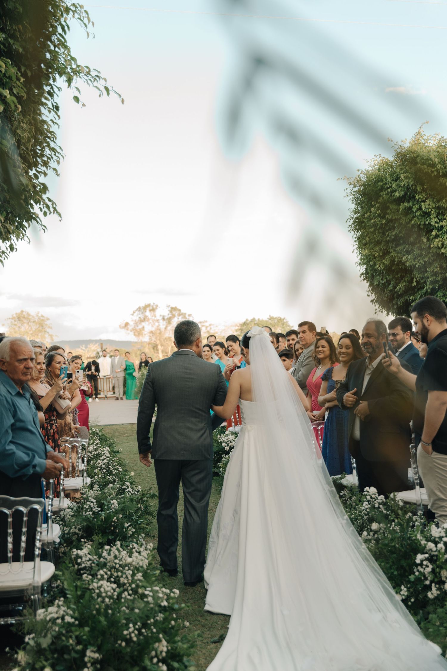 A wedding ceremony with guests lining a flower-decorated outdoor aisle.