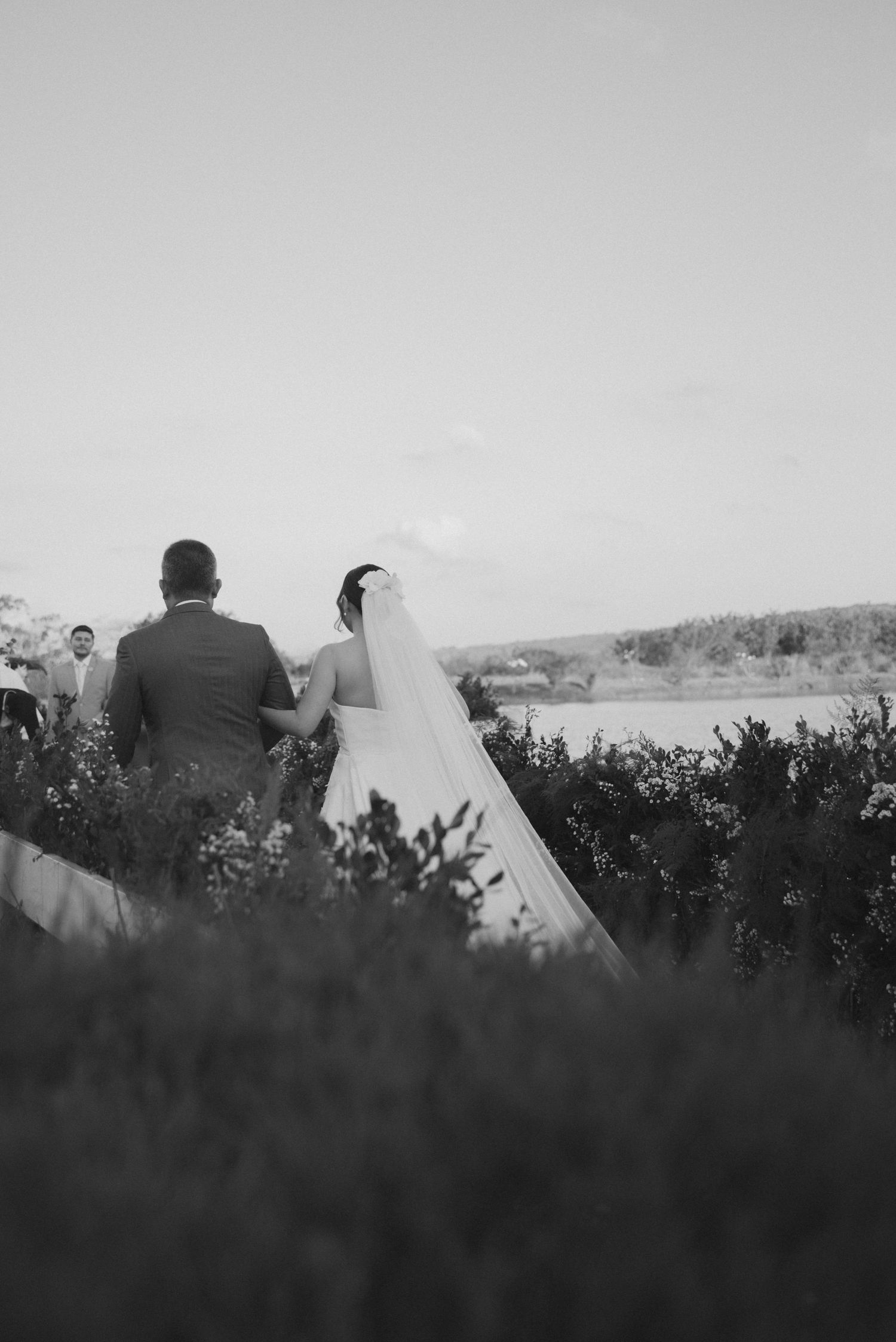 A silhouetted wedding couple standing against a lake view landscape in black and white.