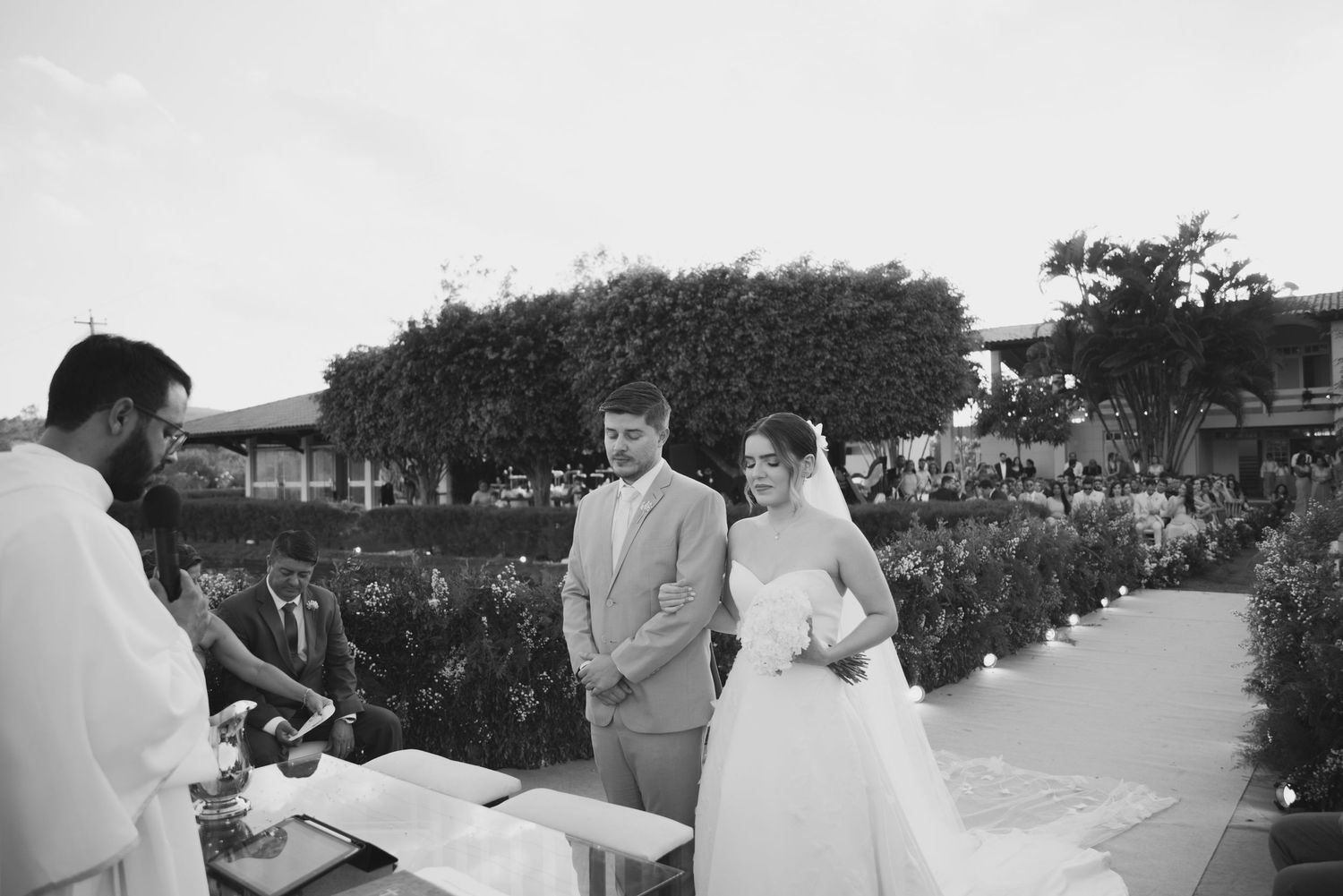 A black and white photo of a wedding ceremony with a couple standing at an outdoor altar.