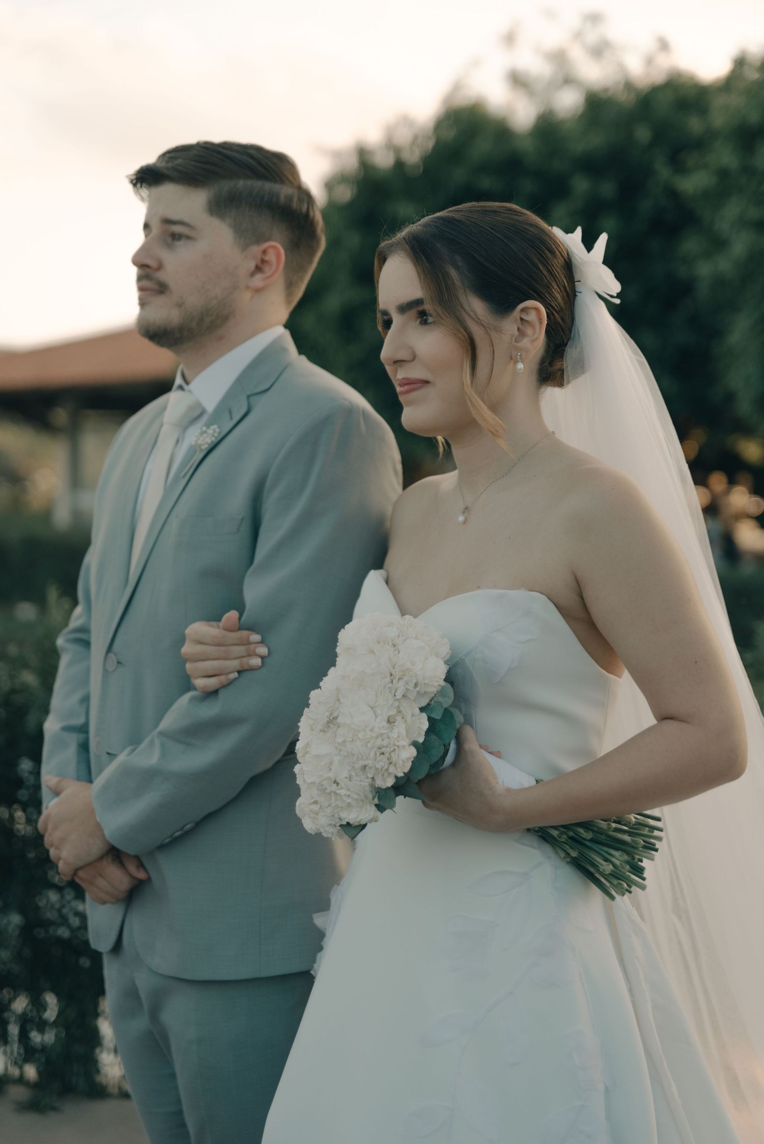 A couple stands together during their outdoor wedding ceremony in formal attire.