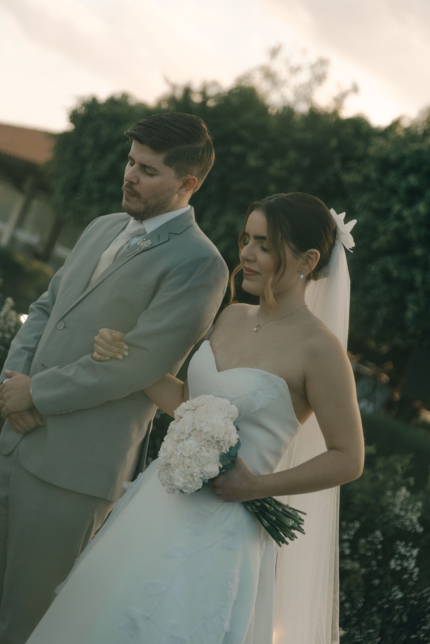 A couple in wedding attire stands before a hedge backdrop during their ceremony.