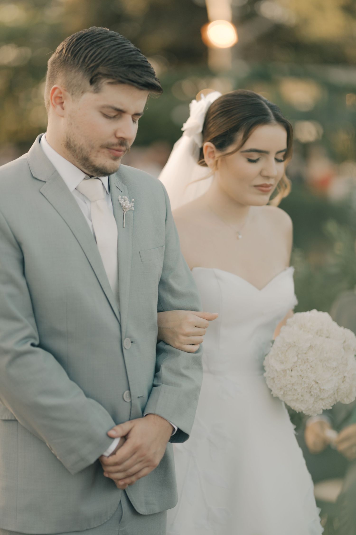 A couple in wedding attire stands together during golden hour at their outdoor ceremony.