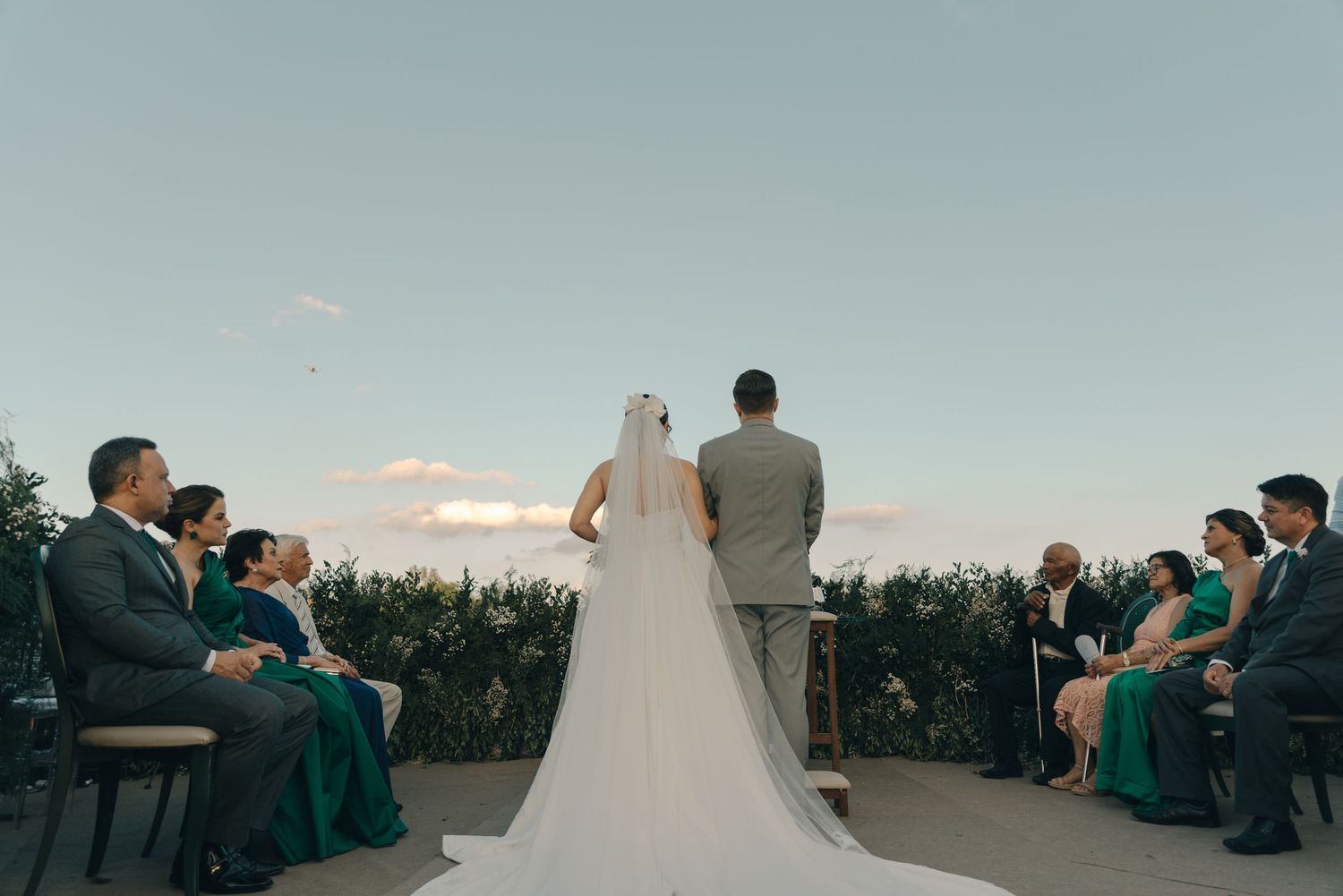 A wedding ceremony taking place outdoors with wedding party members seated and the couple standing at the altar.