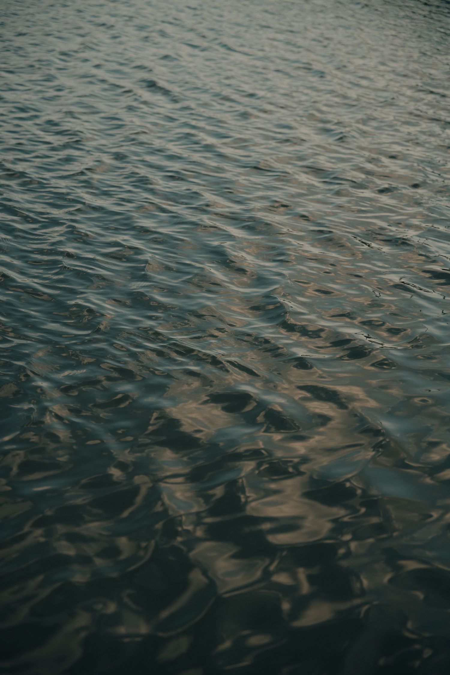 Rippling water surface with light reflections creating a moody, dark texture.