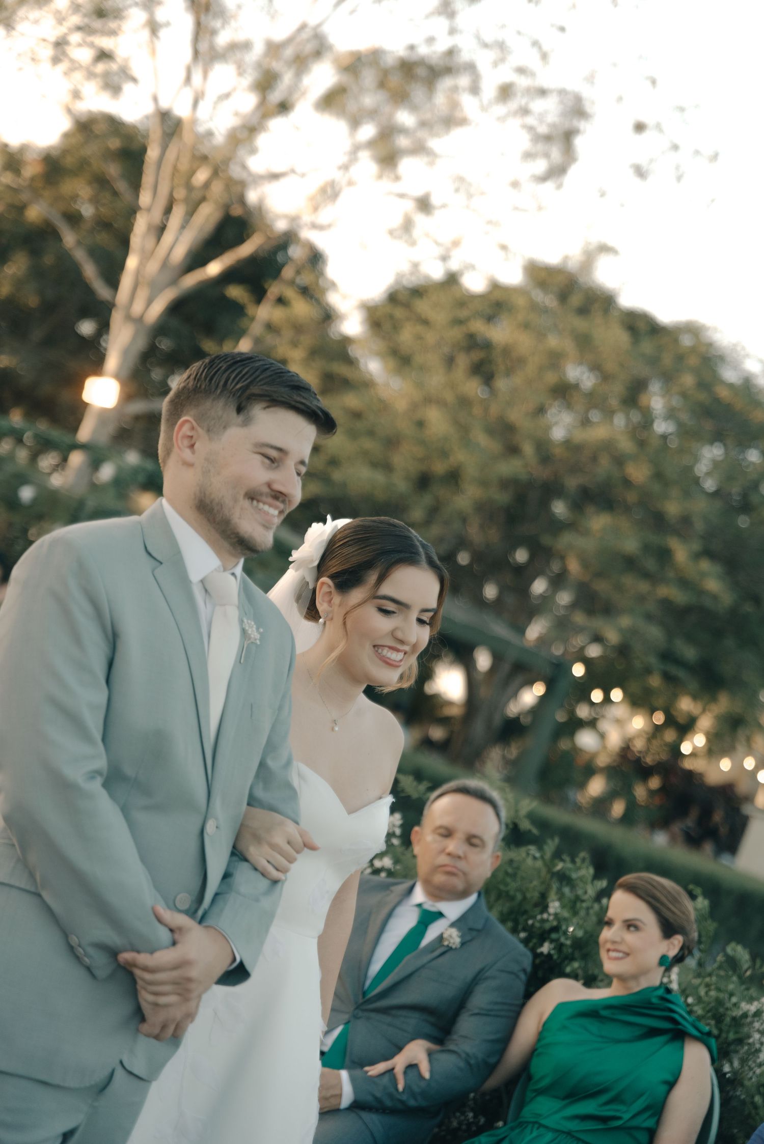 Wedding couple sharing a joyful moment during their outdoor ceremony with guests in green attire.