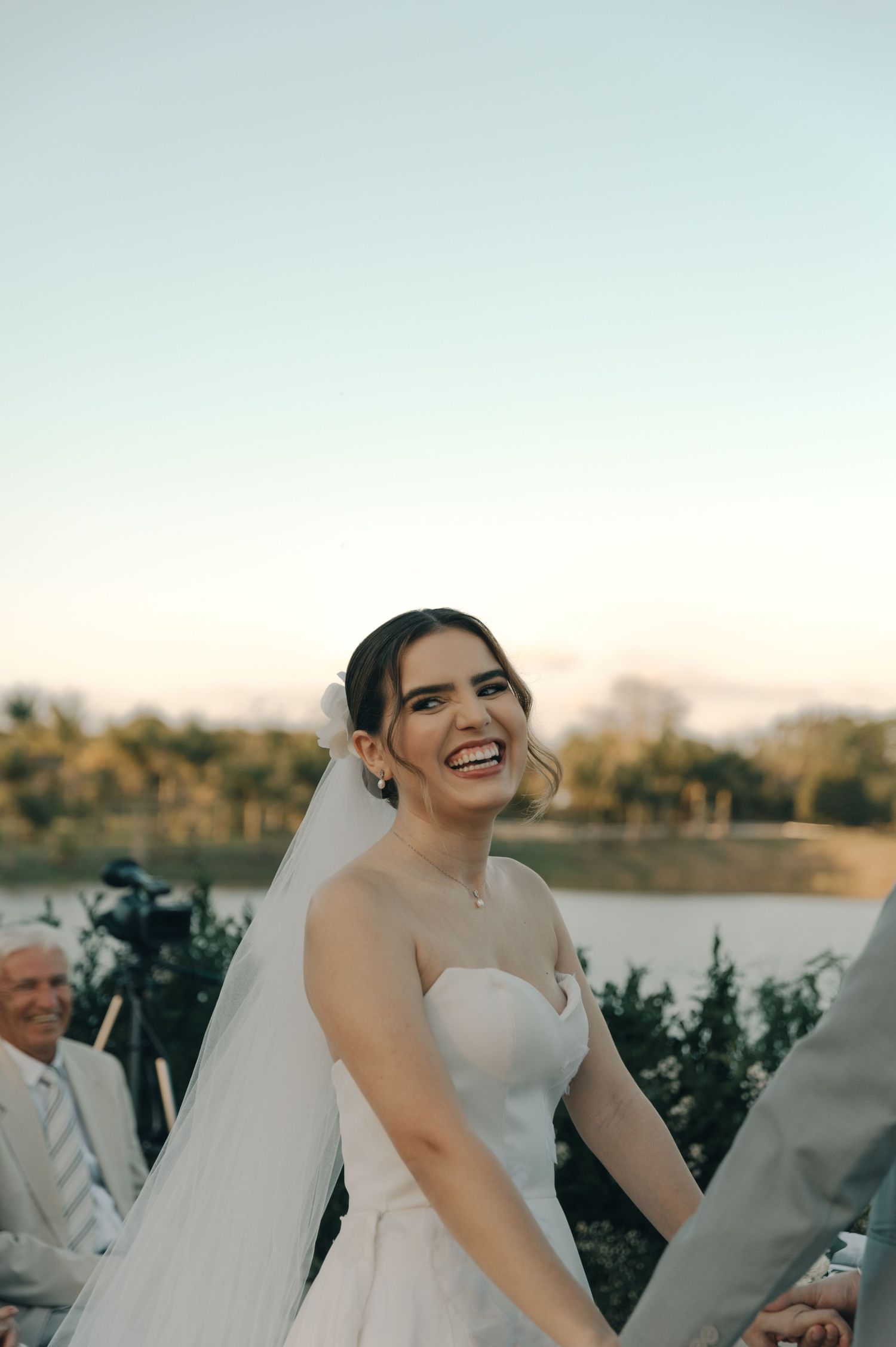 A bride in a strapless wedding gown laughs joyfully during her outdoor ceremony.