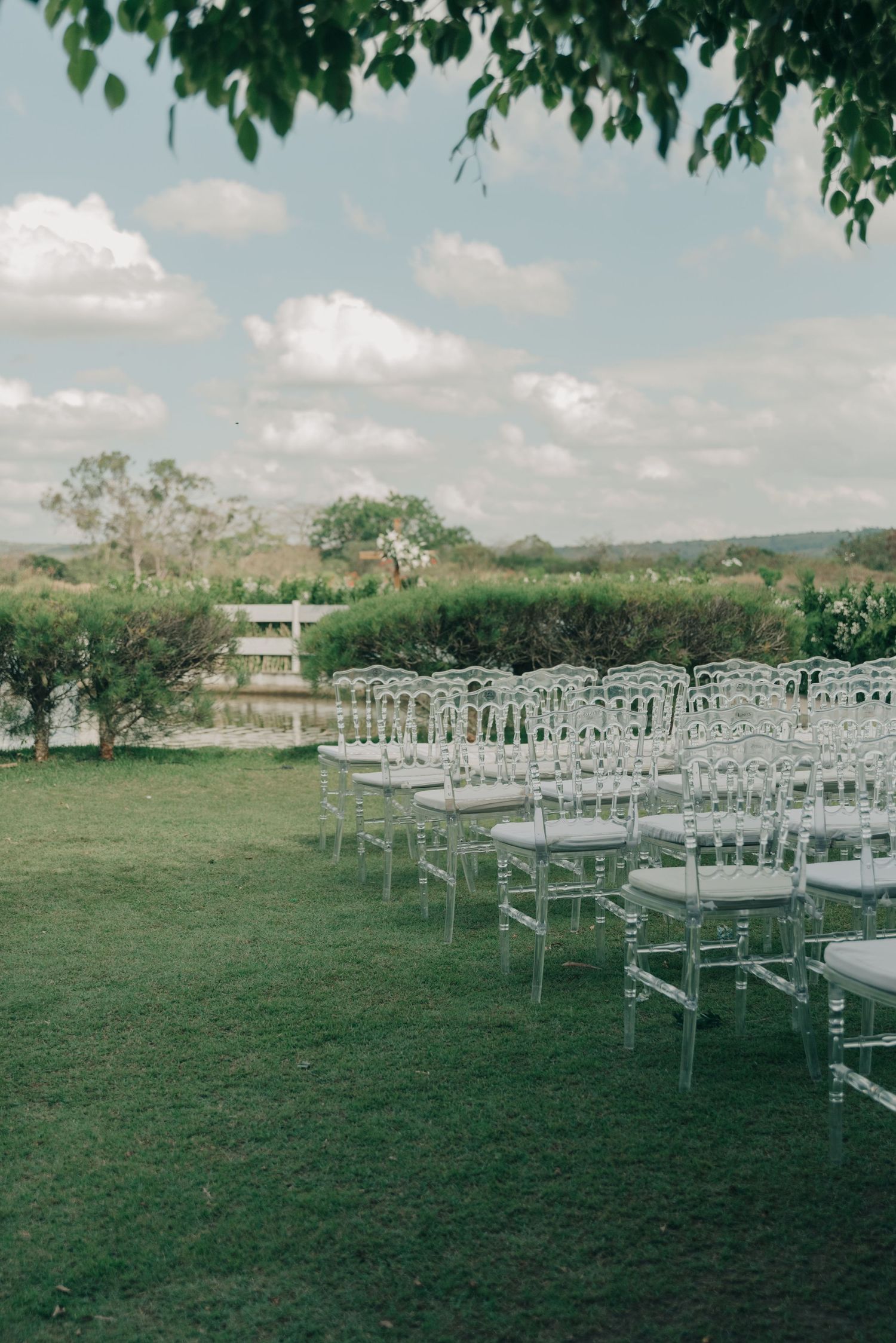 Outdoor wedding ceremony setup with white chairs on a green lawn under cloudy skies.