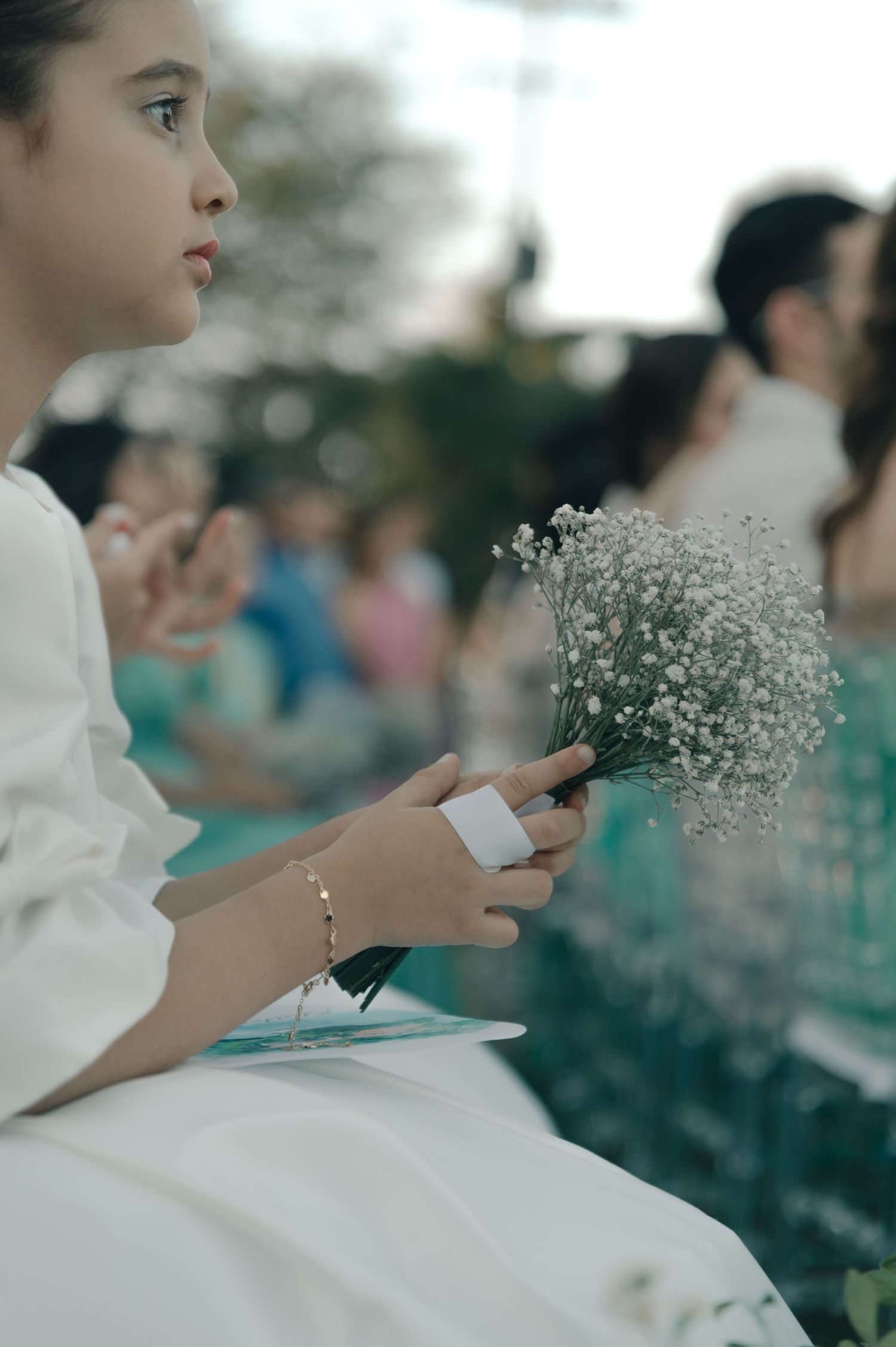 A person in white holds delicate baby's breath flowers at an outdoor event.