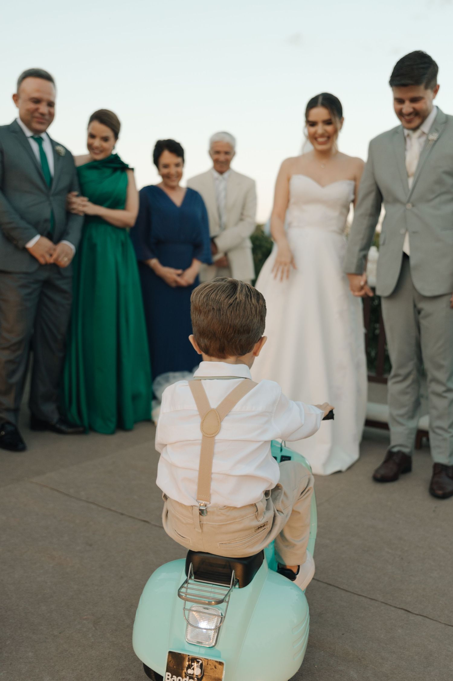 A young child on a mint green toy car looks up at wedding party members.