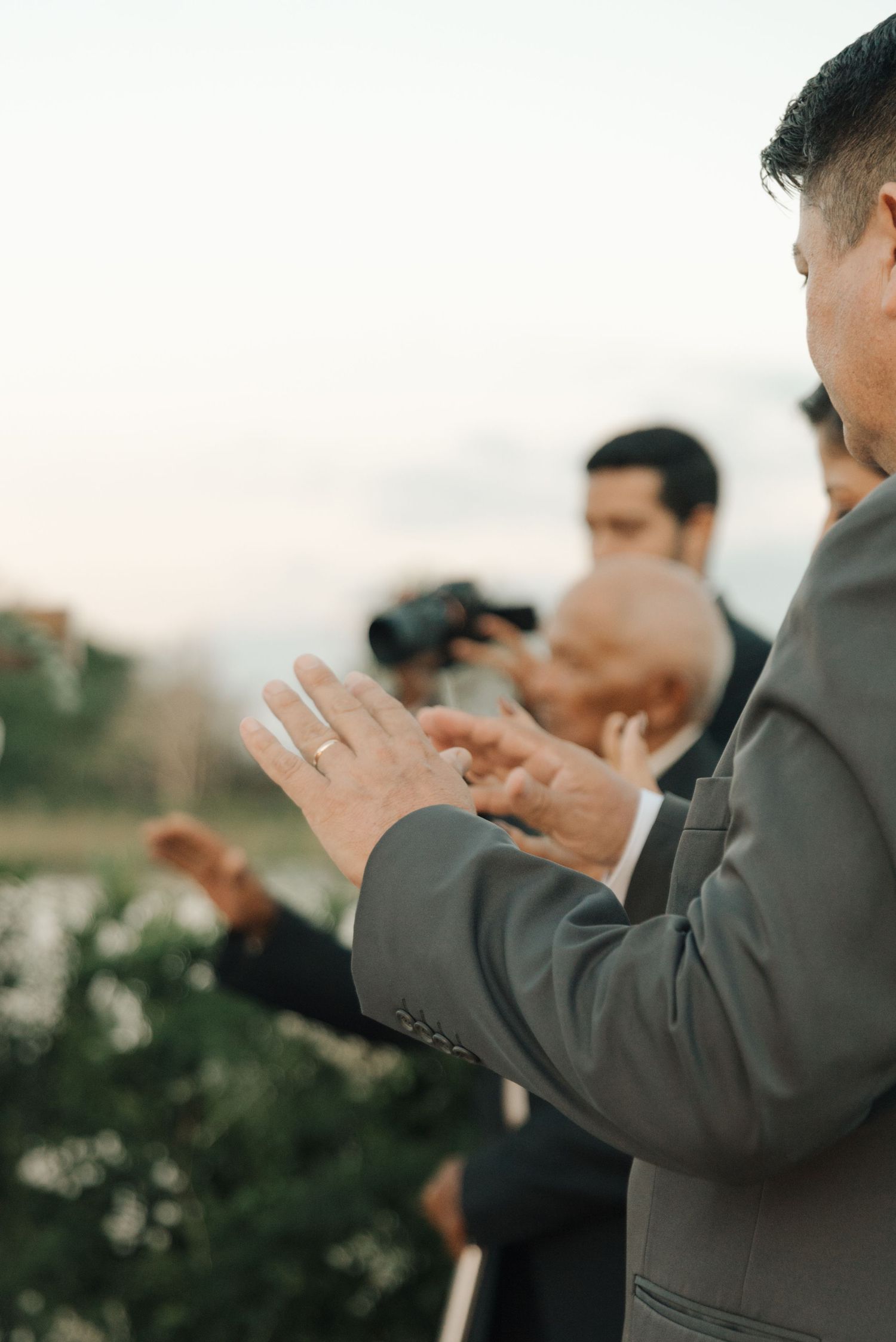 Wedding guests applaud outdoors during a sunset ceremony with lush greenery in the background.