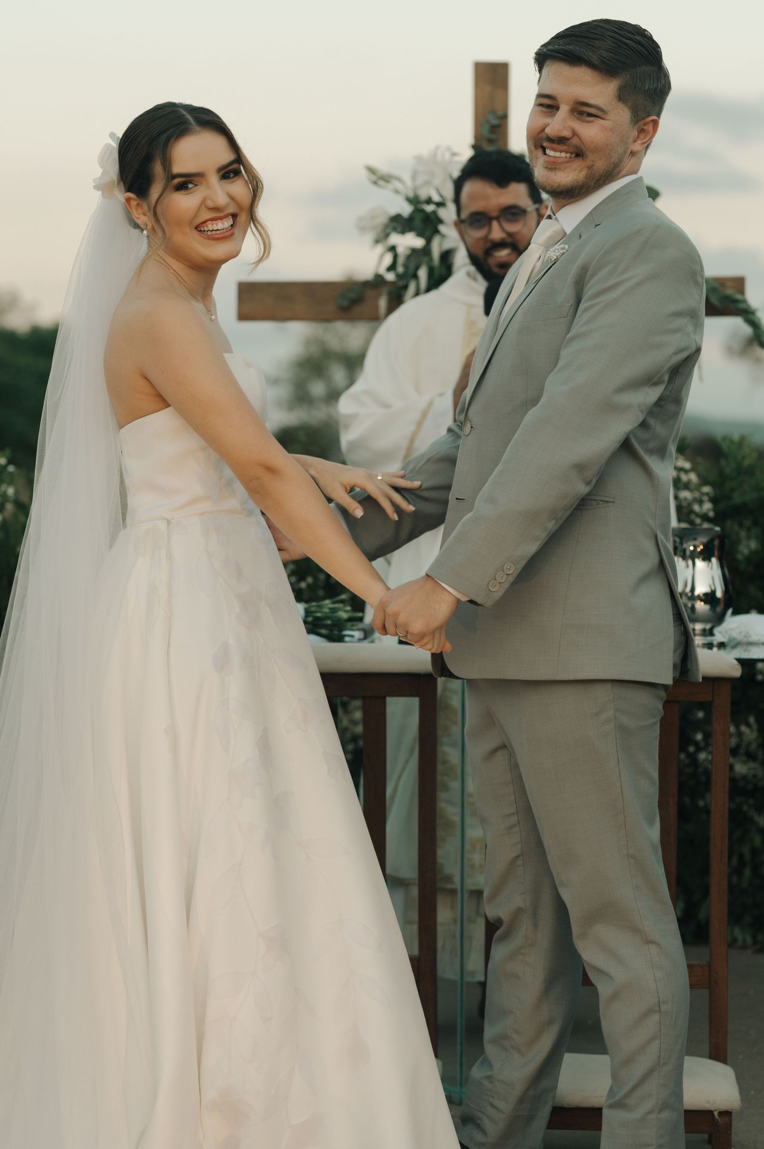Bride and groom hold hands while smiling during their outdoor wedding ceremony.