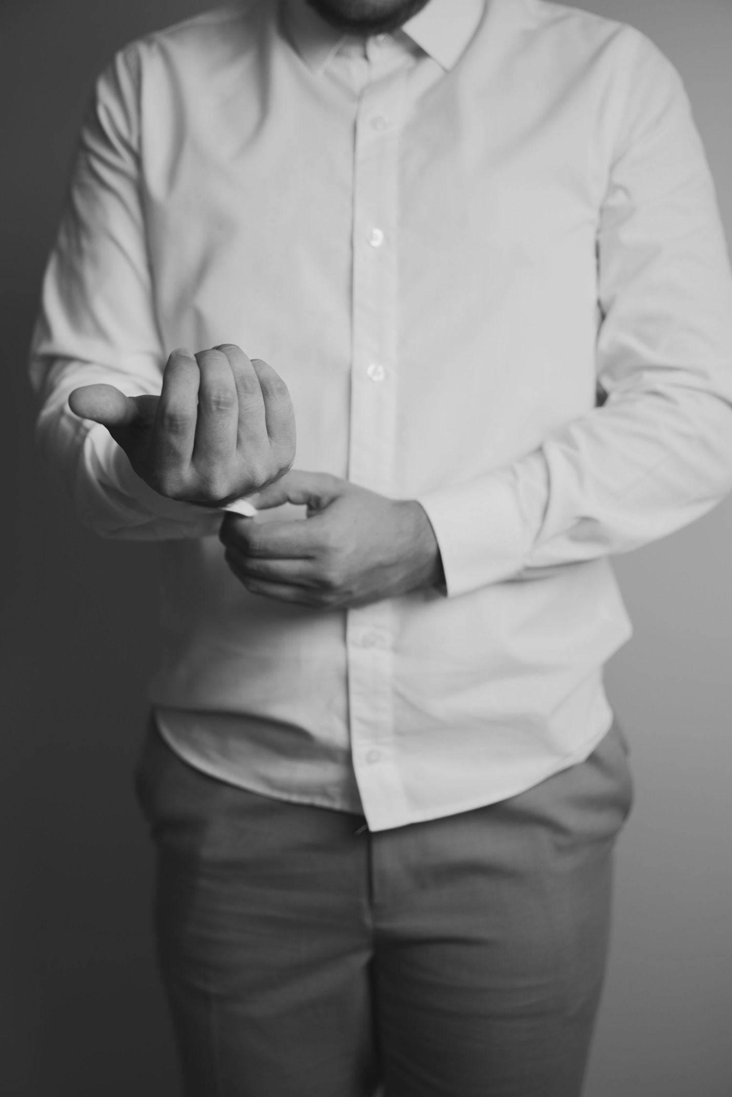 Man in white dress shirt buttoning his cuffs in black and white photography.