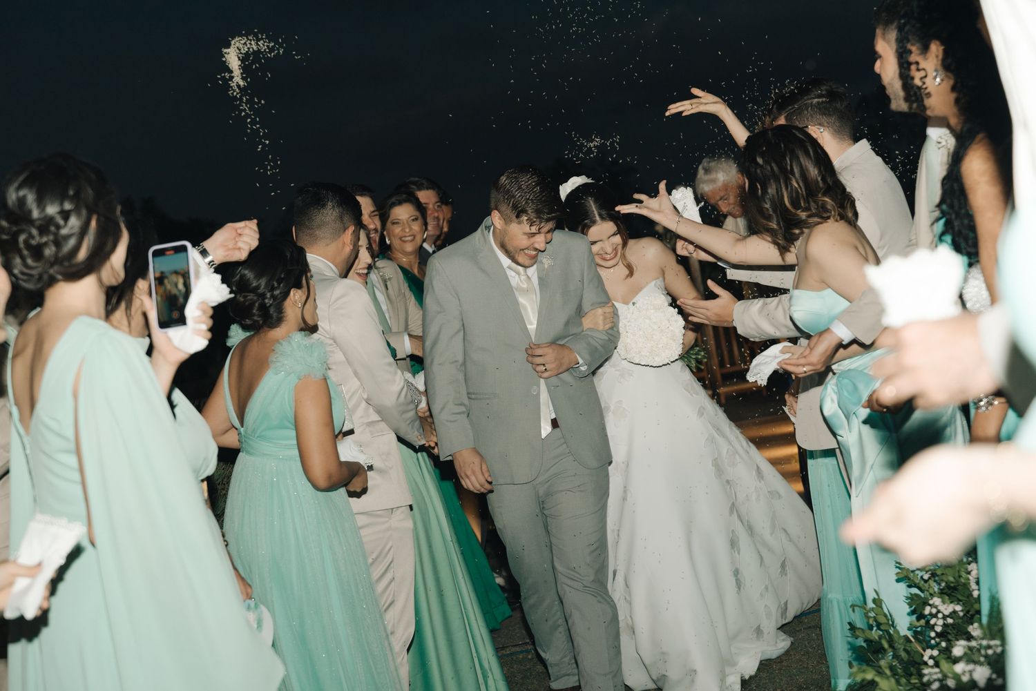Wedding party in mint green dresses and gray suits dancing together on a dark dance floor.