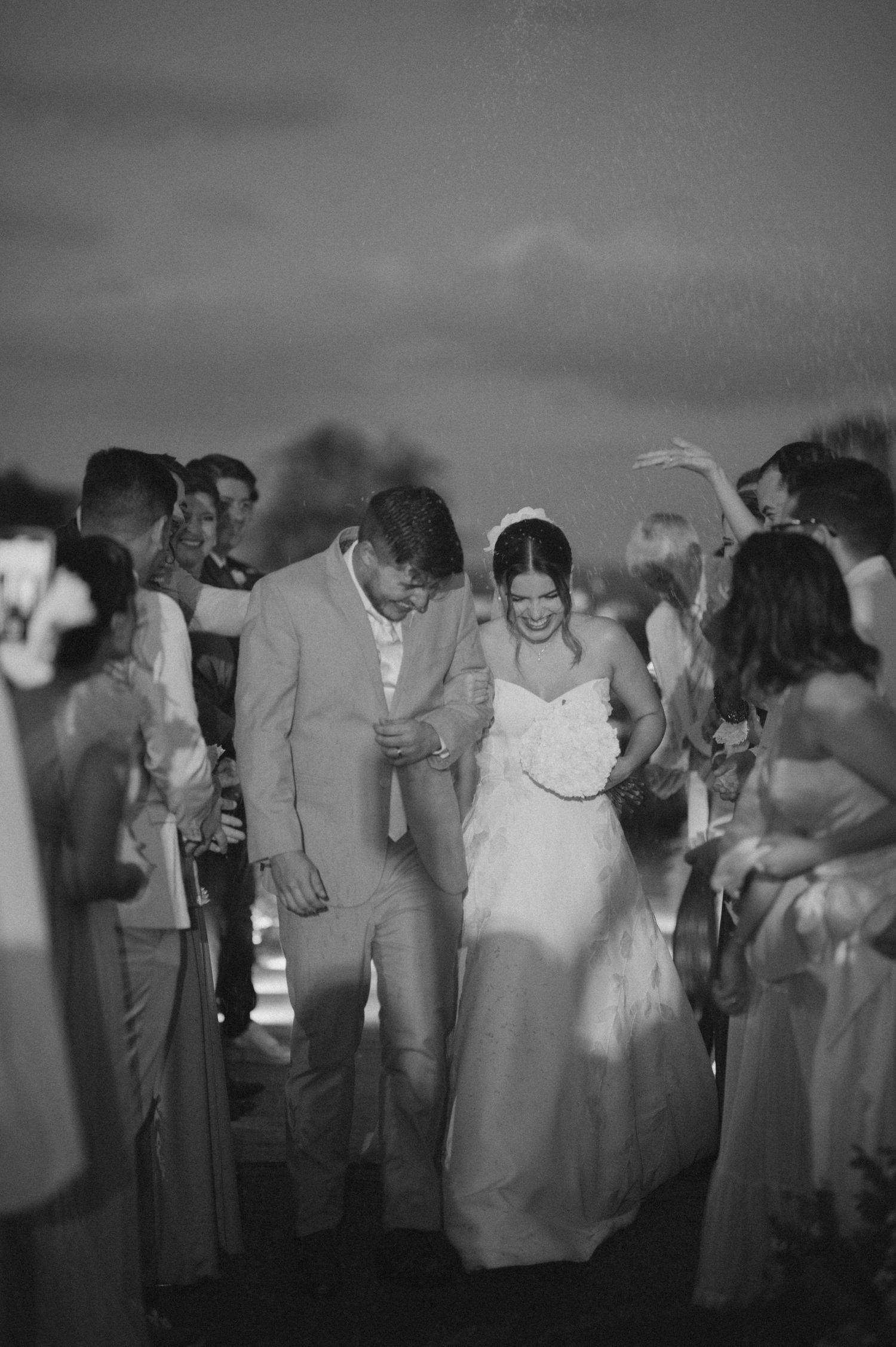 Couple in wedding attire dancing surrounded by guests in a black and white photo.