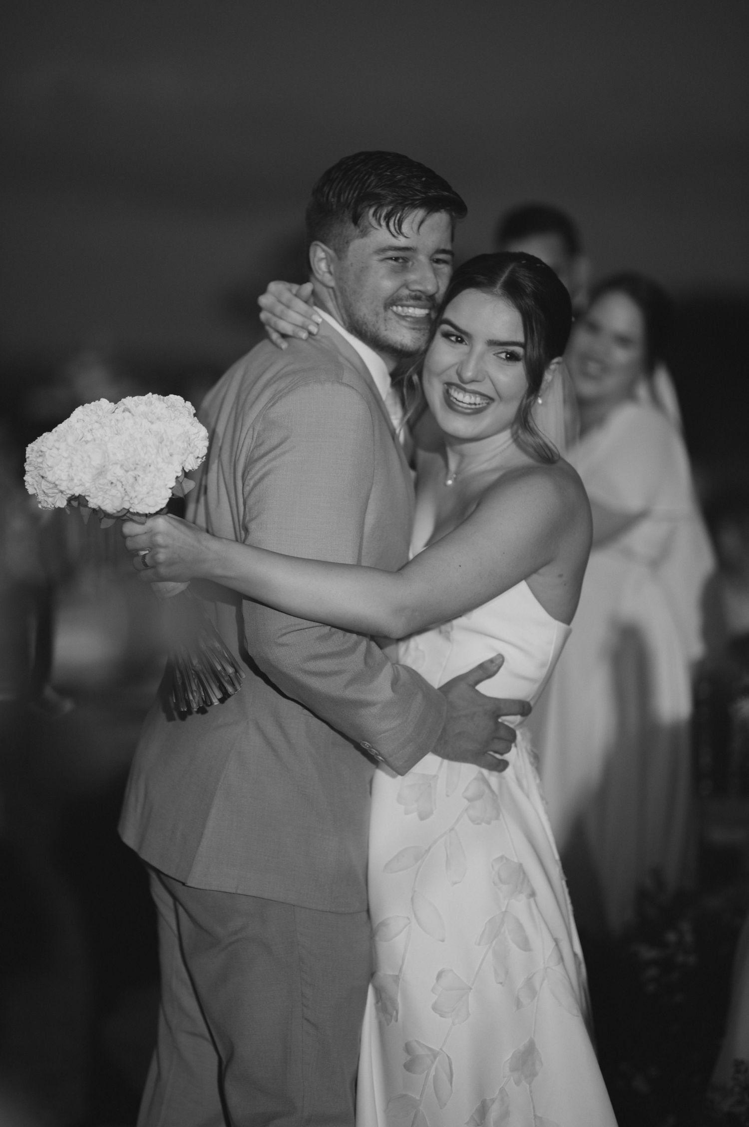Newlyweds share an intimate embrace with white bouquet in black and white photo.