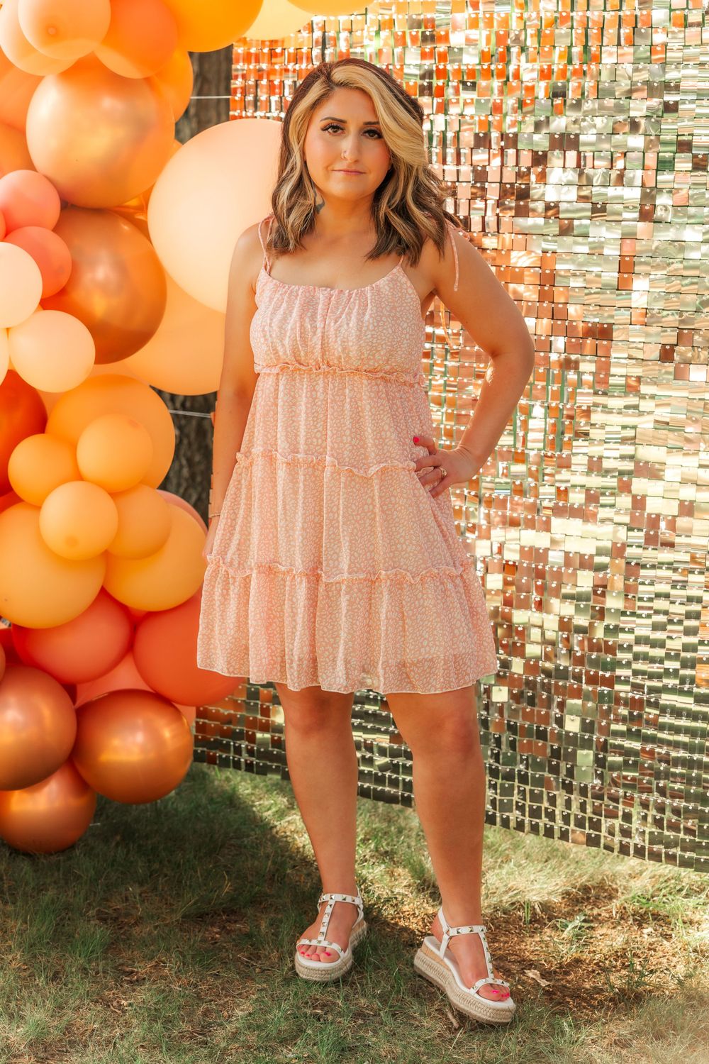 Woman in pink tiered dress poses against balloon arch and metallic backdrop.