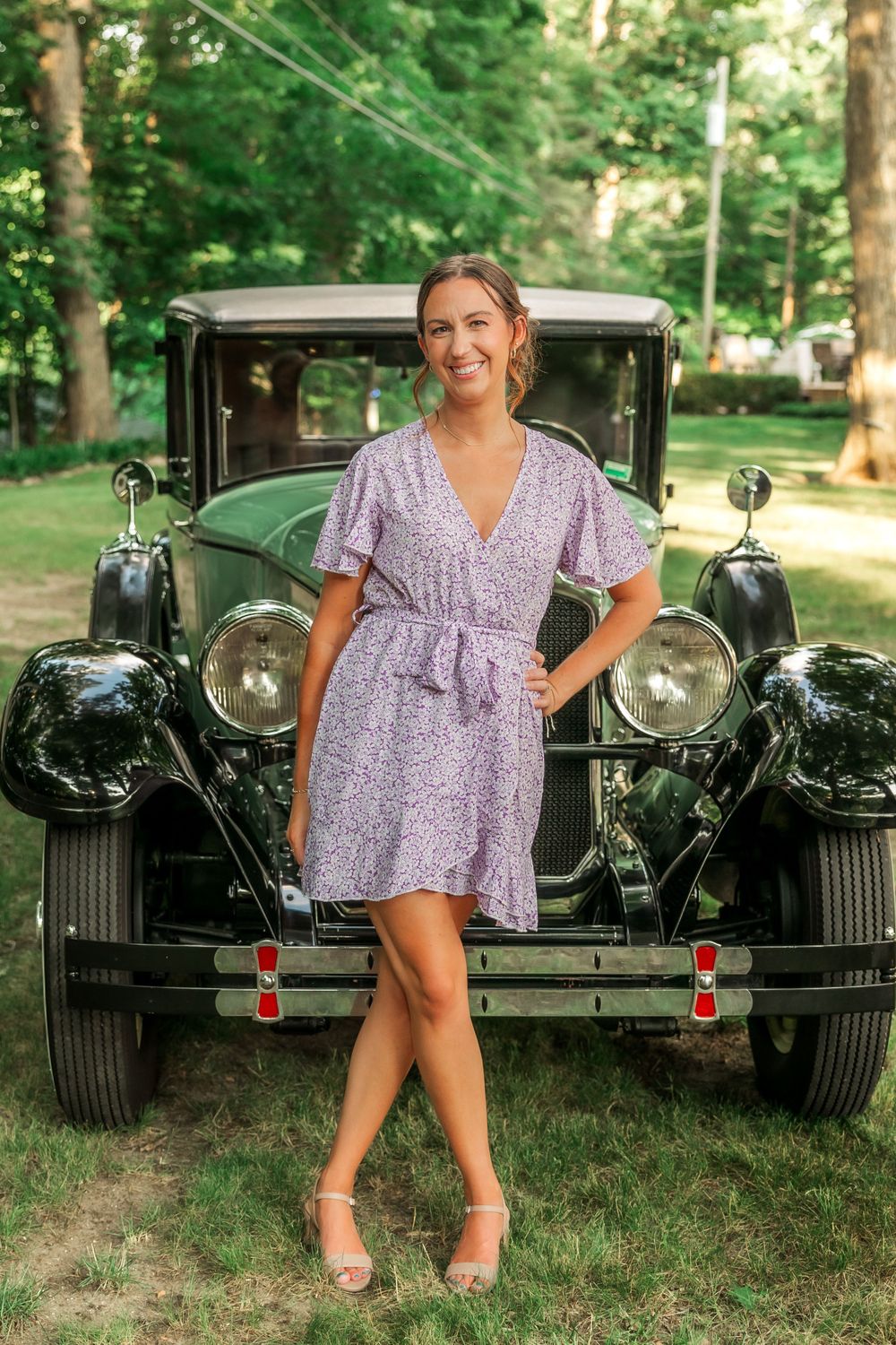 Classic vintage car serves as backdrop for summer fashion photography in a wooded setting.