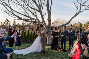 Outdoor wedding ceremony under bare winter trees with guests gathered around the wedding couple.