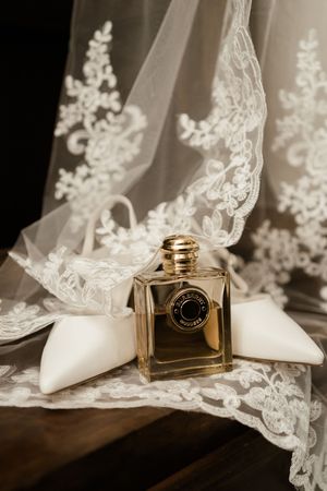Elegant gold perfume bottle rests on delicate white lace veil against neutral background in a wedding styled photo series.