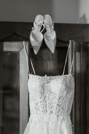 A white lace wedding dress and bridal shoes displayed elegantly against a dark wooden background.