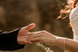 Hands exchanging wedding rings during an intimate ceremony with warm golden sunlight filtering through.